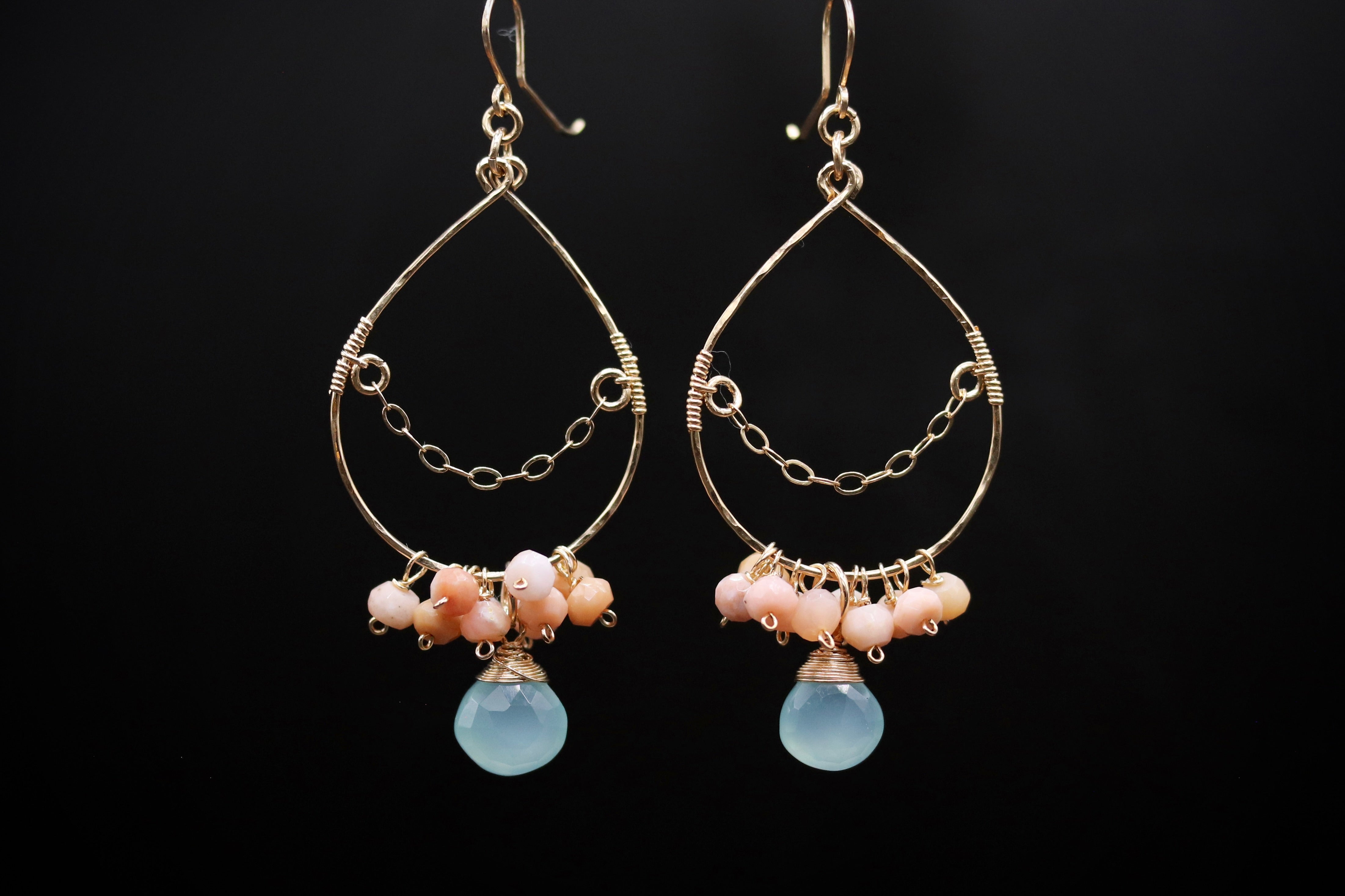 A pair of elegant earrings with a teardrop-shaped design, featuring a chain and a blue stone bead at the bottom.