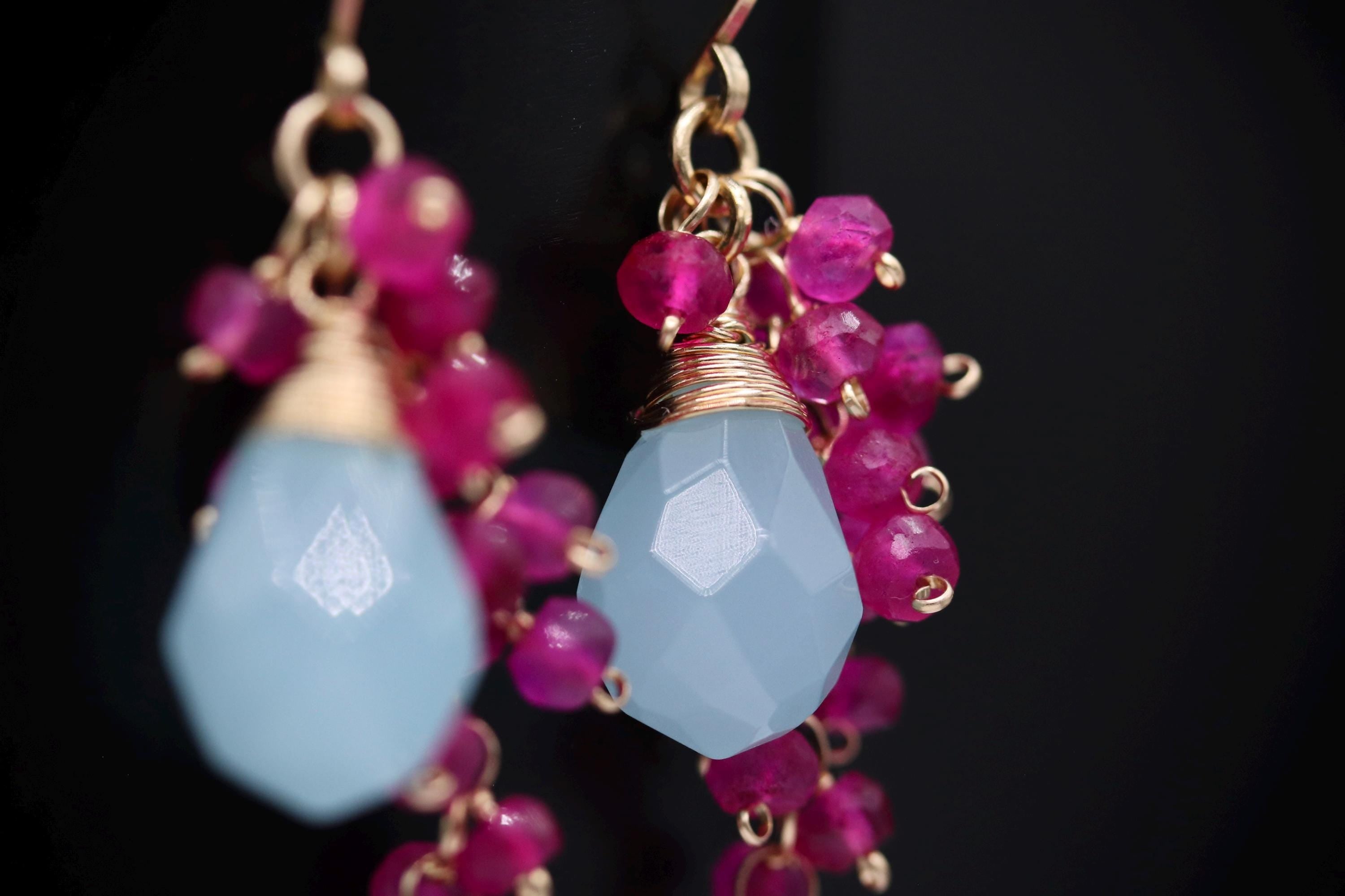 A pair of earrings with a blue gemstone and pink gemstone beads, set against a dark background.