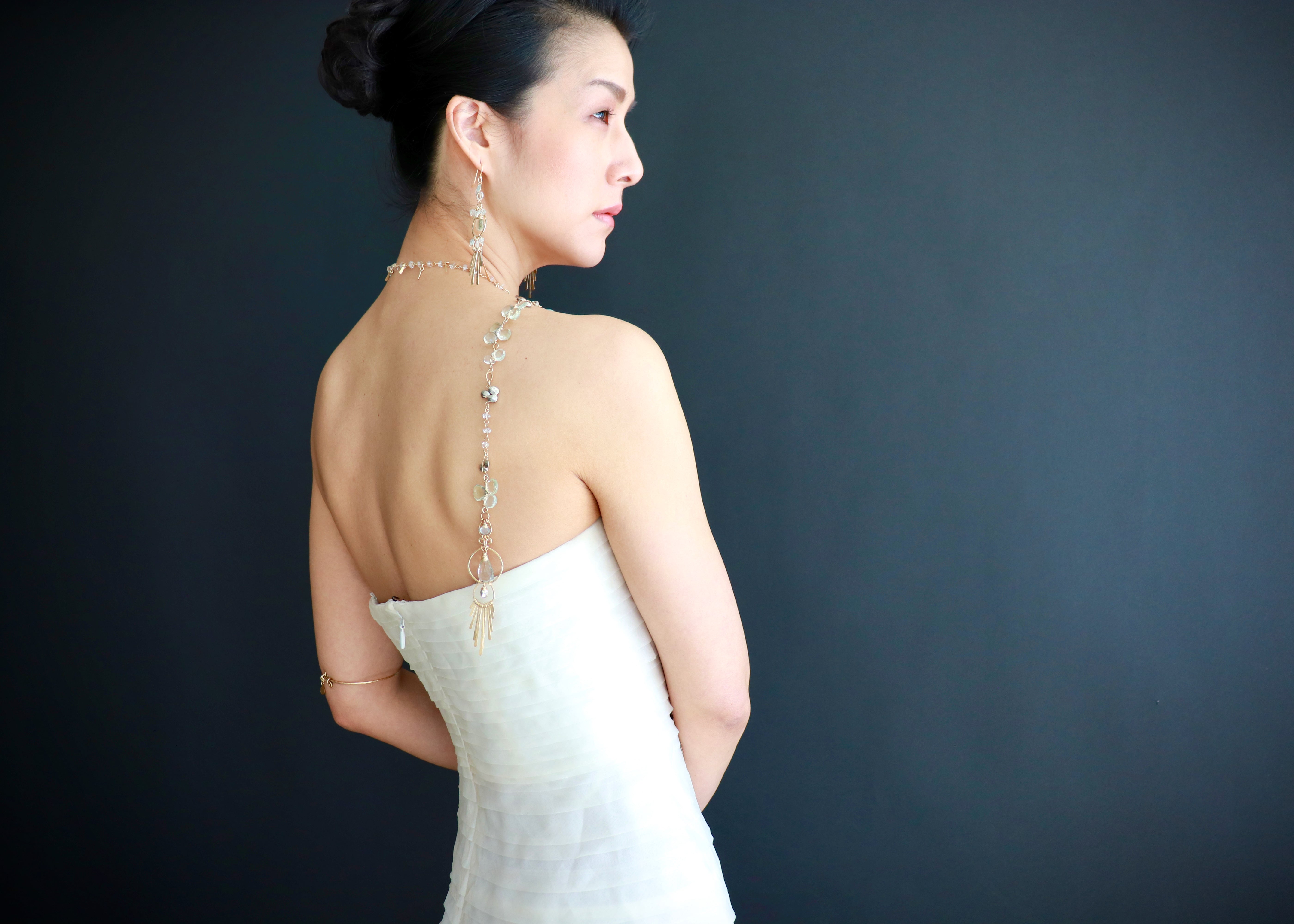 A woman in a white strapless dress stands against a dark background, her back to the camera.