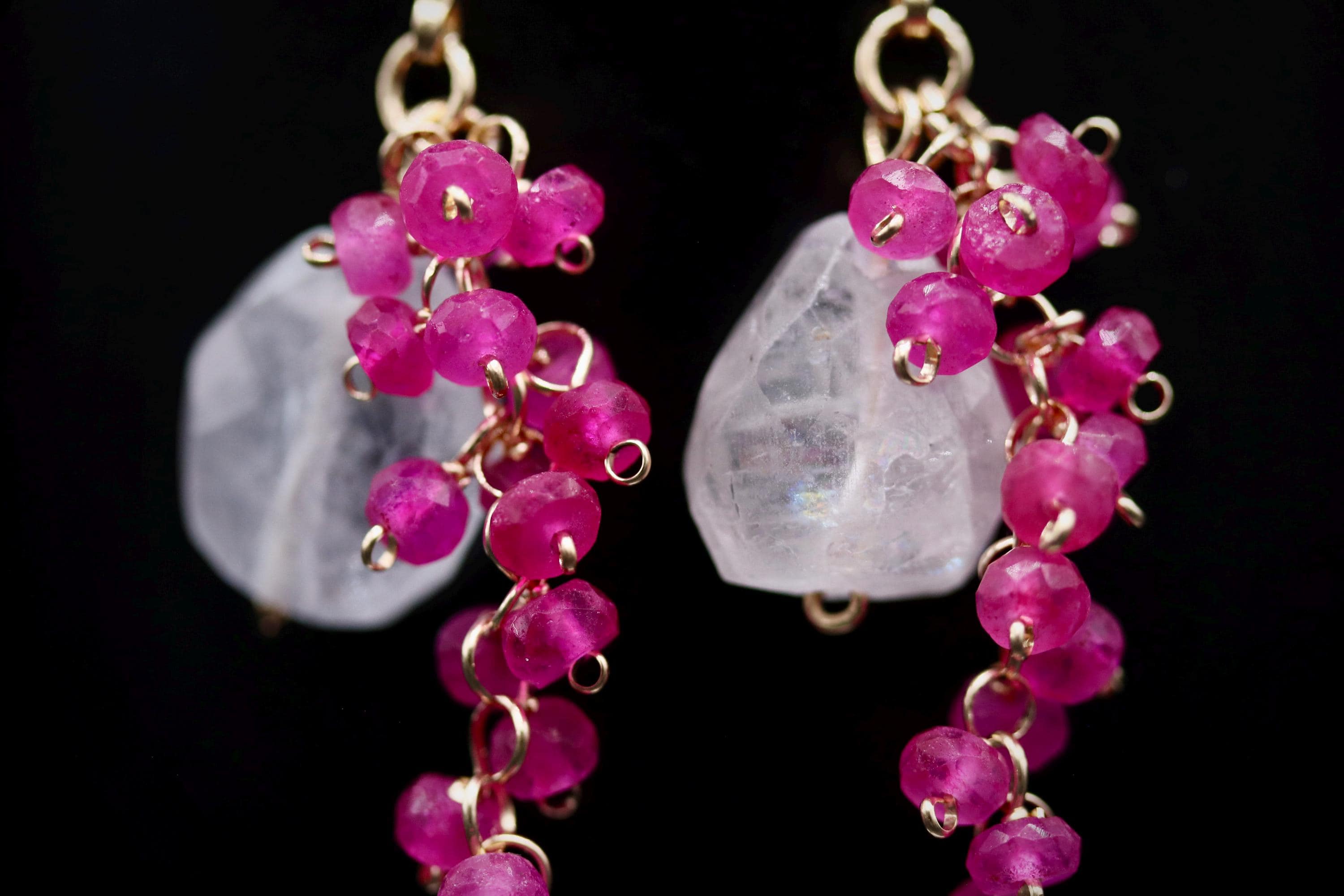 A pair of earrings with clear gemstones and pink beads hanging from the ear hooks.