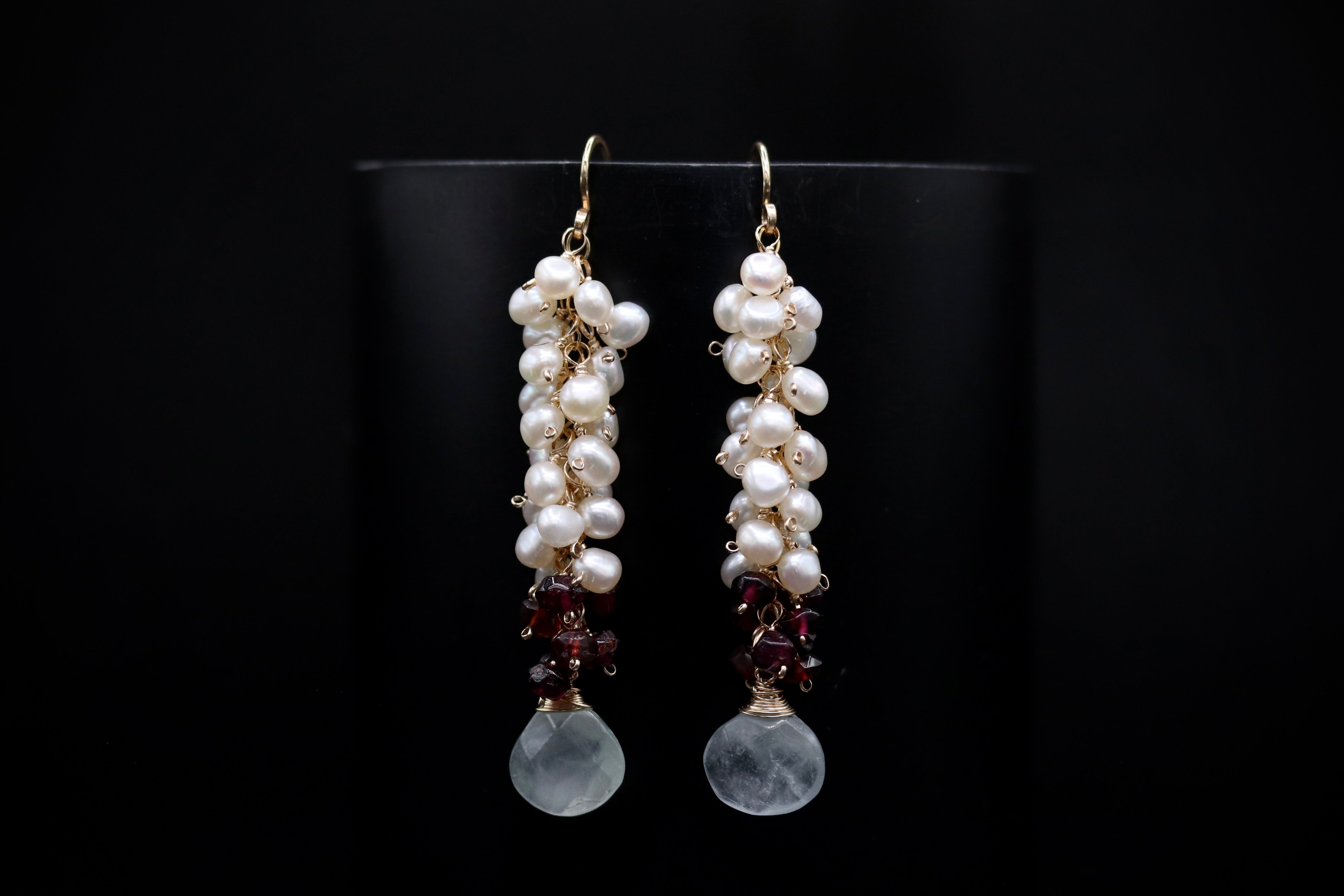 A pair of elegant earrings with white pearls and maroon gemstones hanging from the bottom.