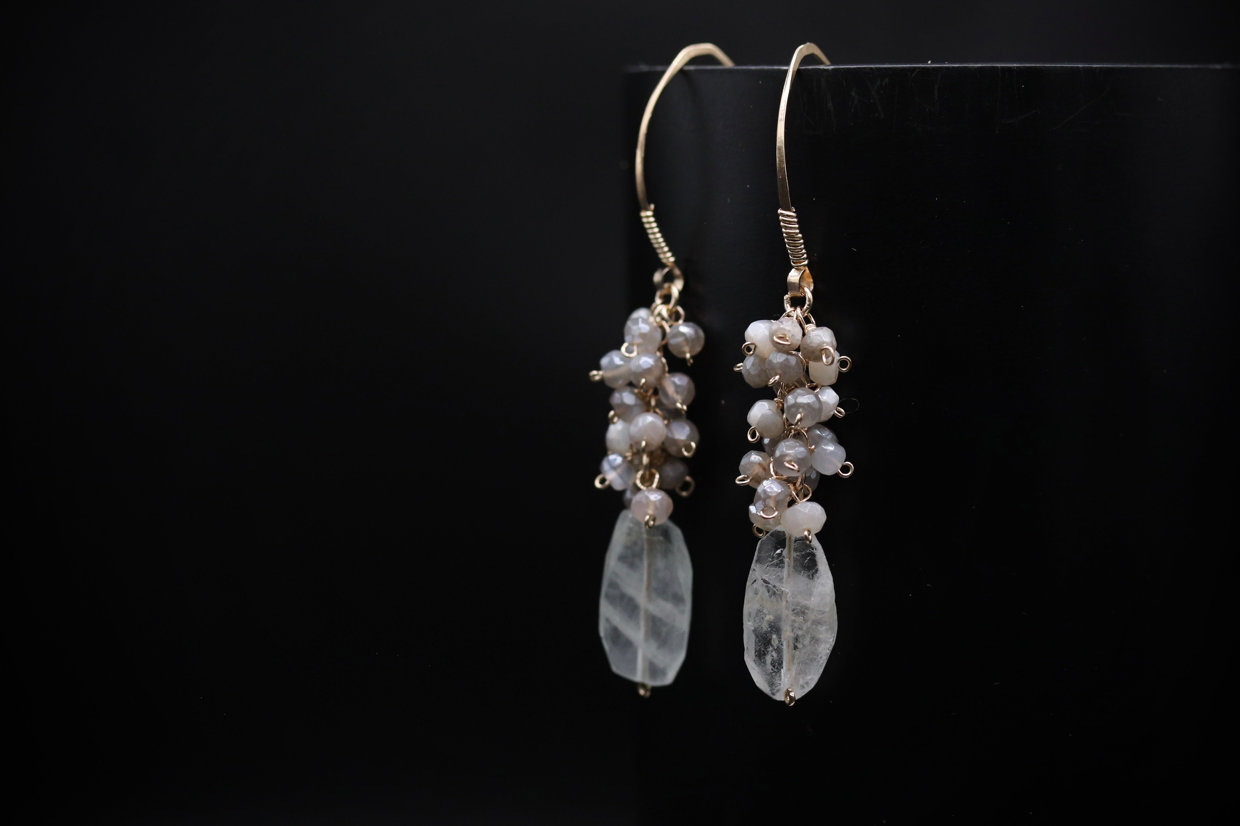 A pair of elegant earrings with clear crystal stones and pearl-like accents, displayed against a dark background.
