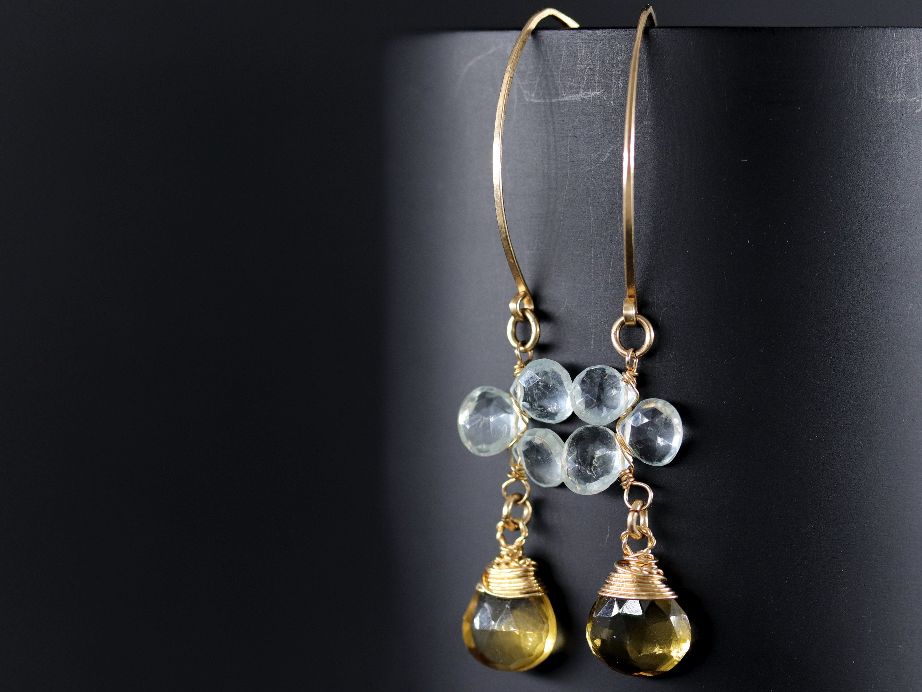 May include: Gold hoop earrings with a cluster of light blue gemstones and two teardrop shaped yellow gemstones hanging from the bottom.