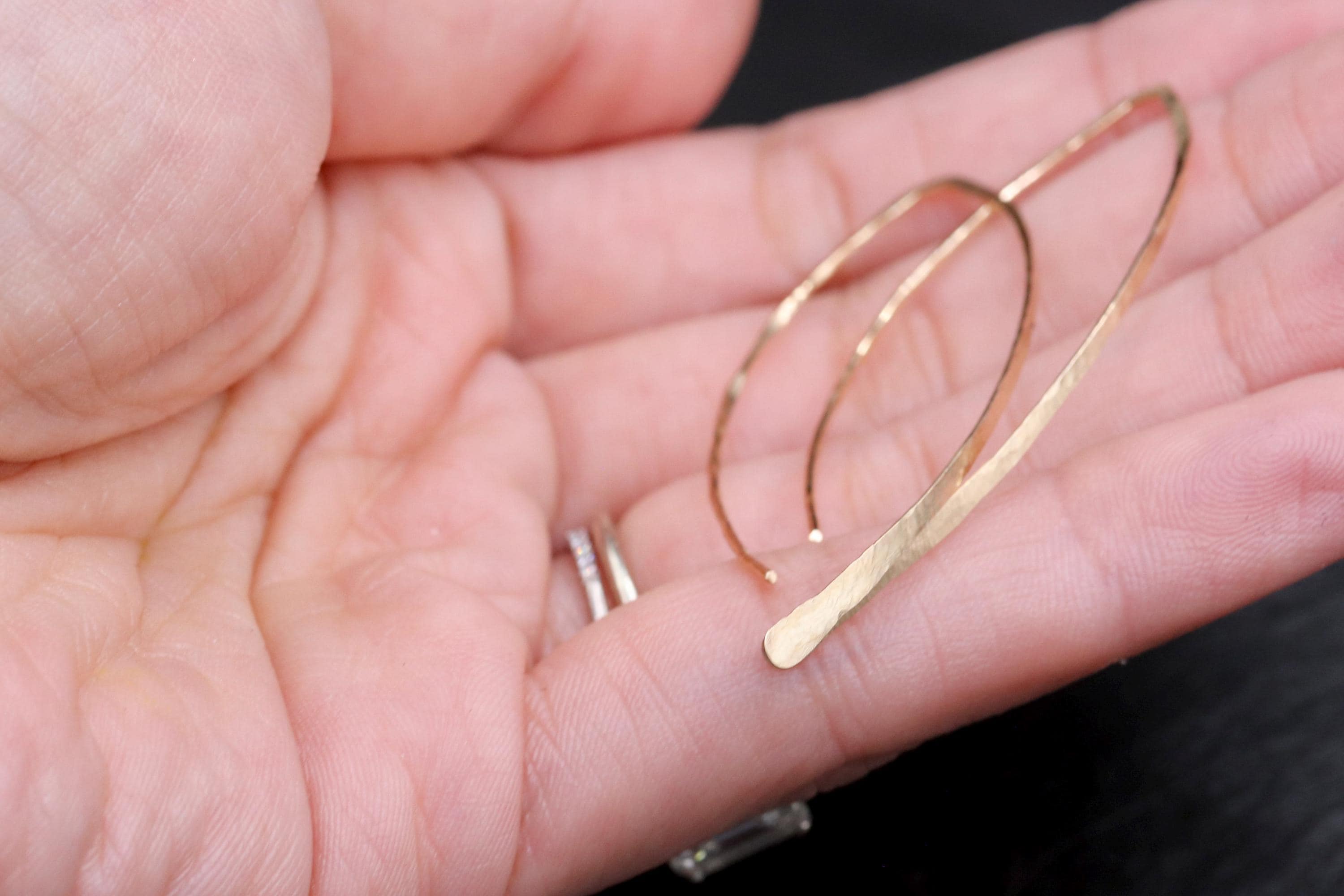 A close-up image of a person's hand holding a gold-colored earring.