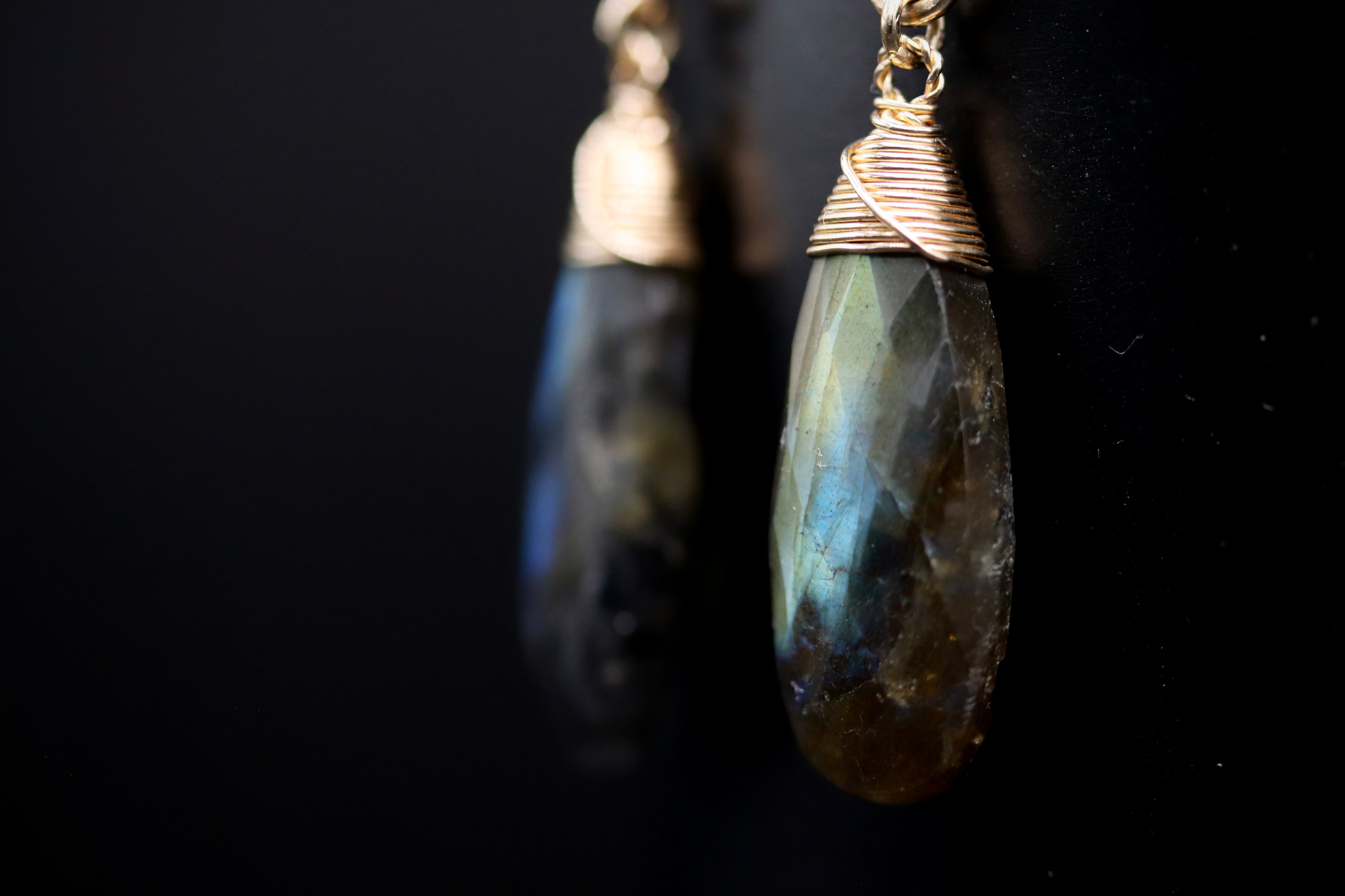 A close-up view of a pair of dangling earrings with a dark stone pendant.