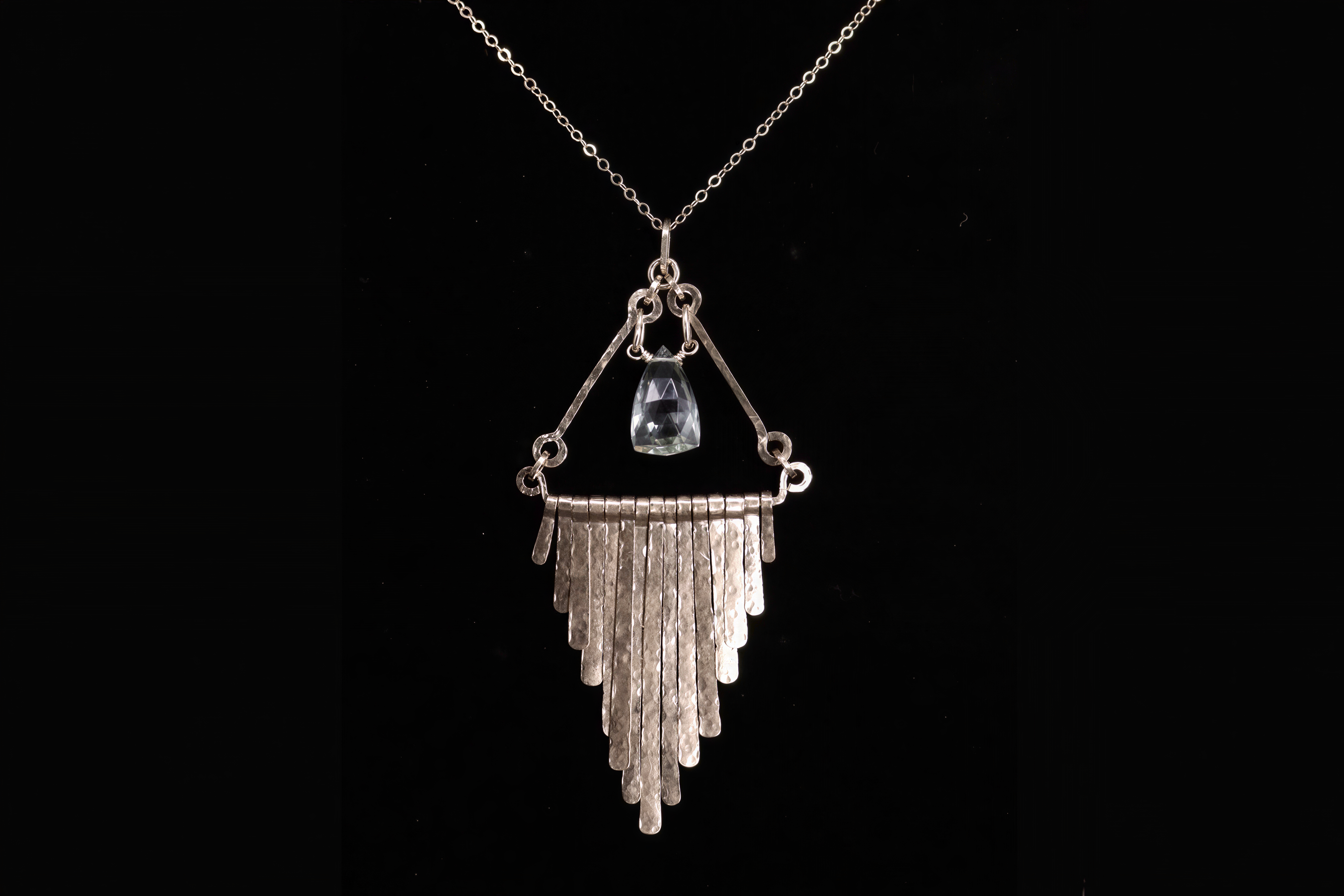 A silver necklace with a pendant featuring a clear gemstone and a cascading metal design.