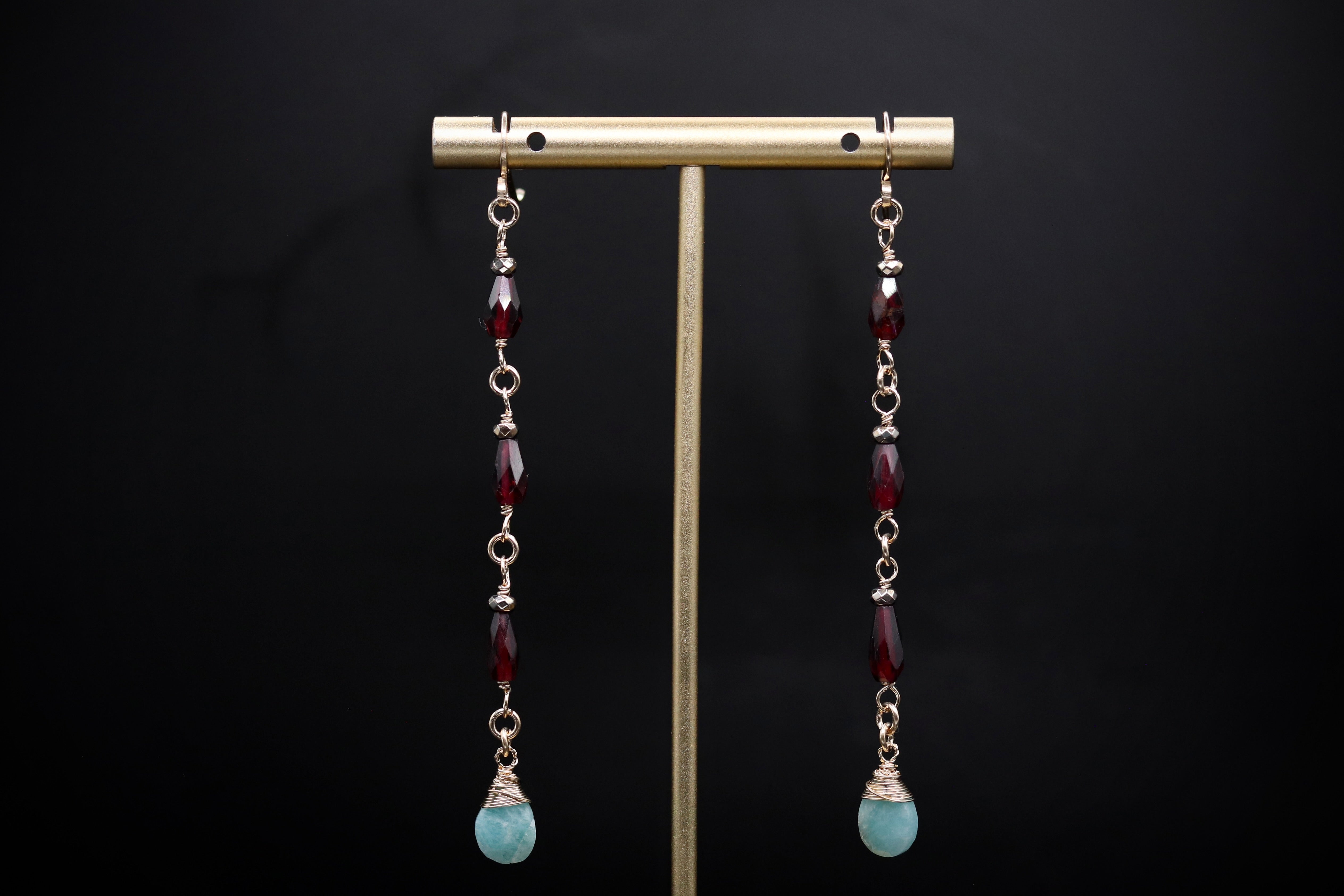 A pair of earrings with red and aqua-colored beads hanging from a gold-colored metal stand against a black background.