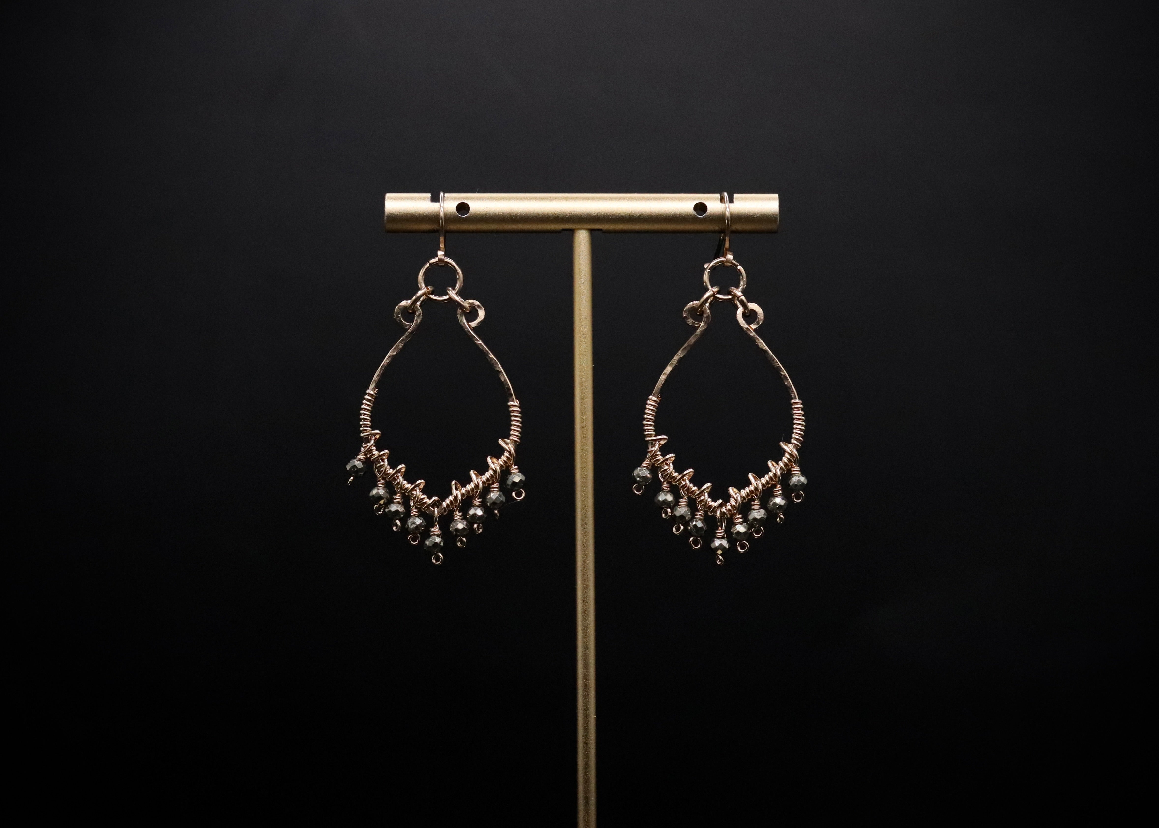 A pair of gold earrings with dangling beads is displayed on a gold stand against a black background.