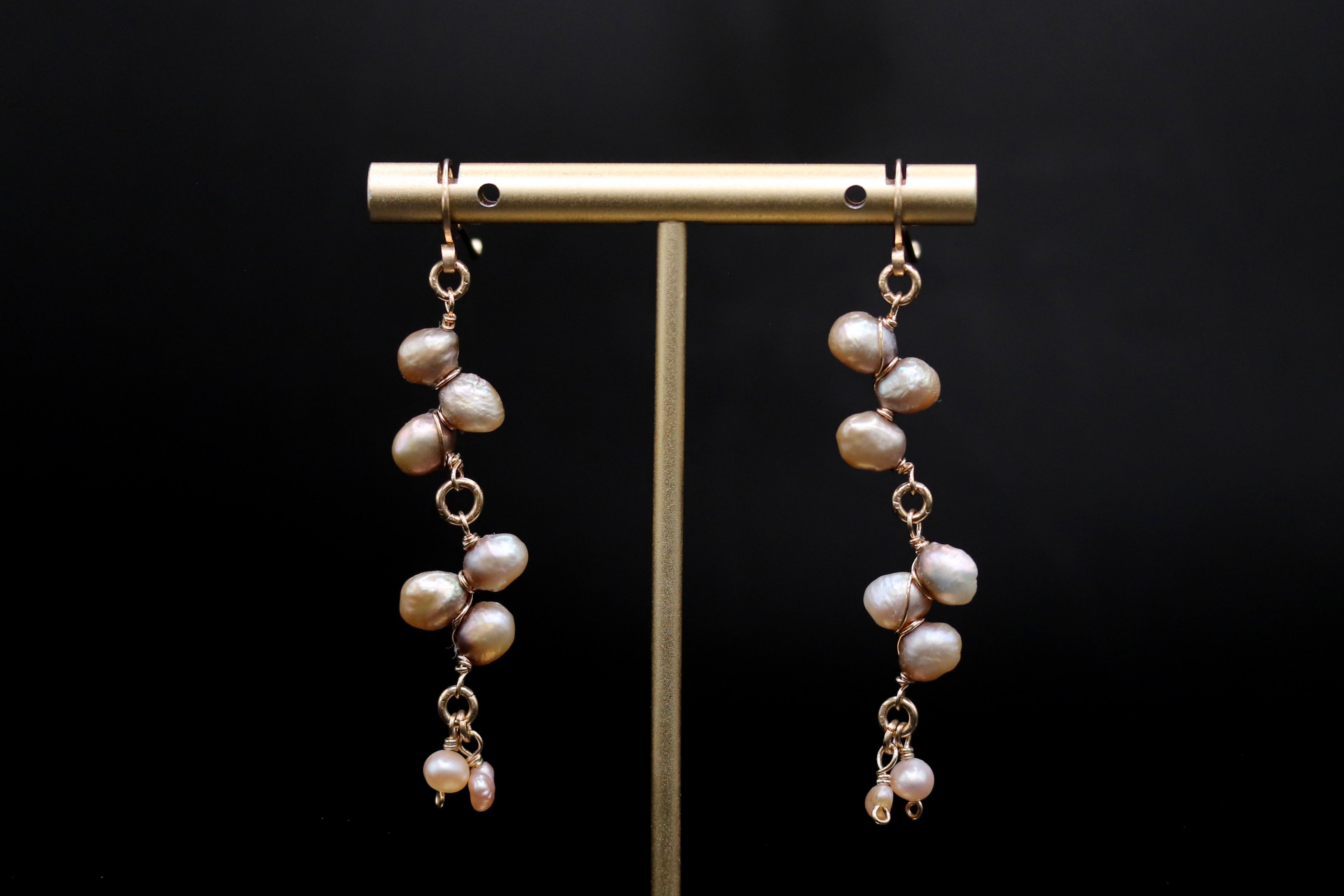 A pair of earrings with multiple strands of pearls hanging from a gold-colored metal stand against a black background.