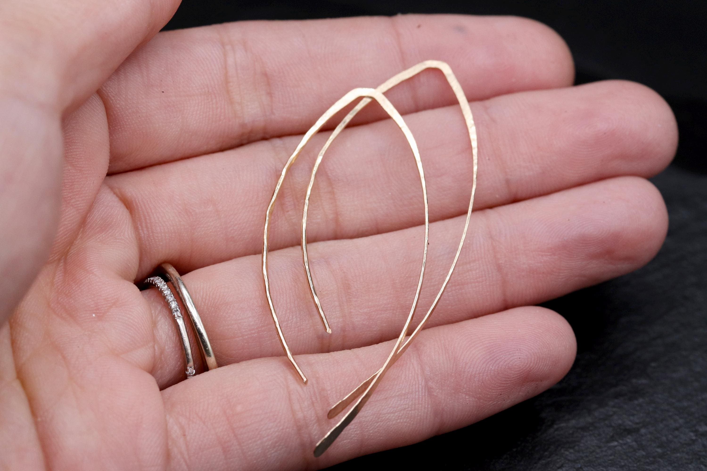 A hand holding a pair of gold earrings against a dark background.
