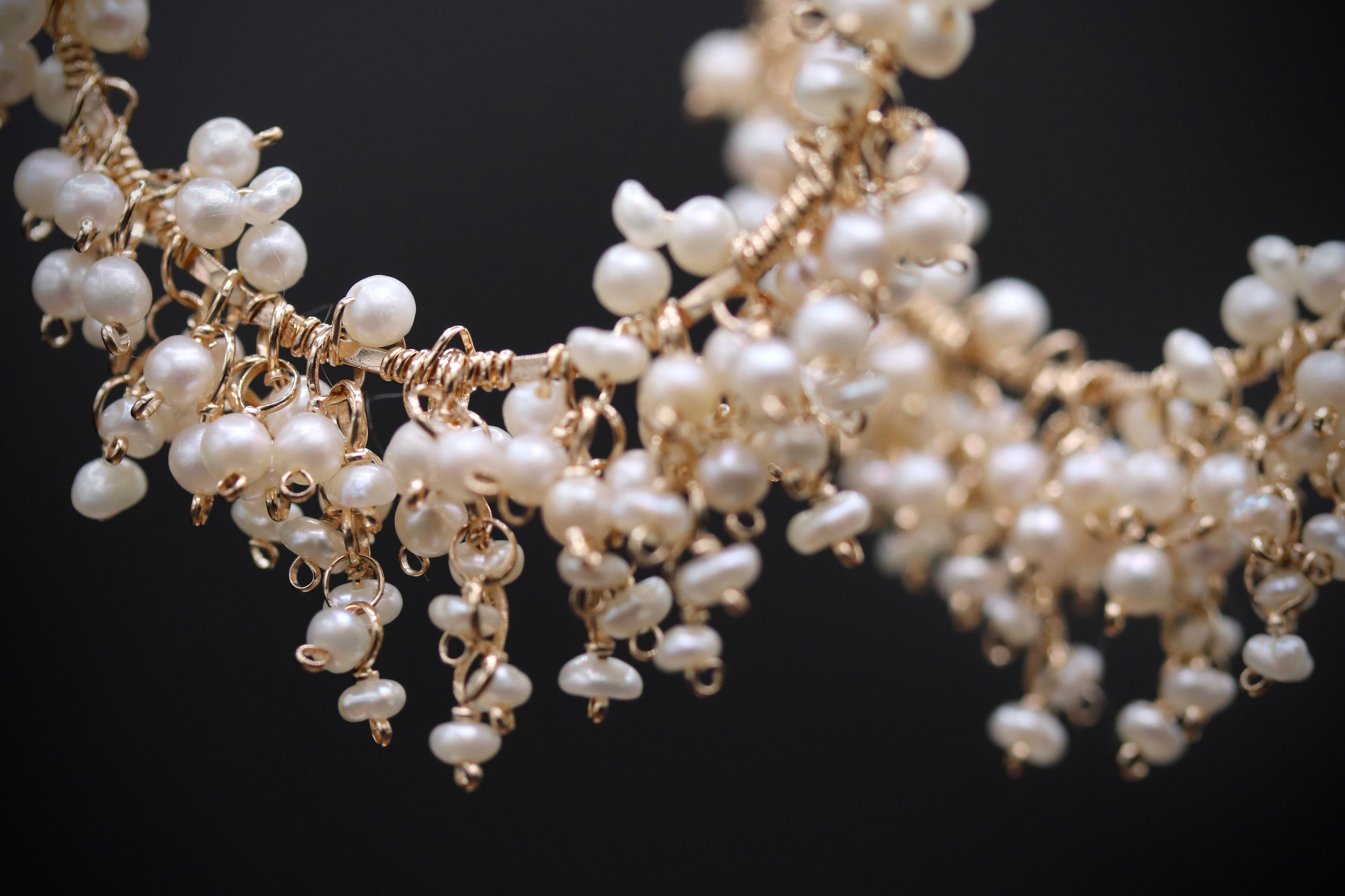 A close-up view of a delicate, intricate necklace made of small, white pearls and gold-colored metal.