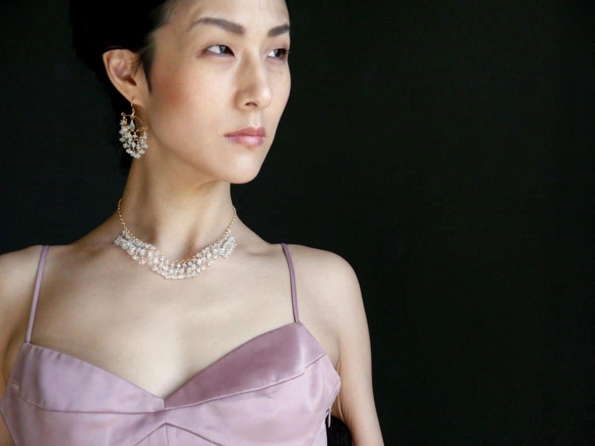 May include: A woman wearing a light pink sleeveless dress with a delicate pearl necklace and matching earrings.