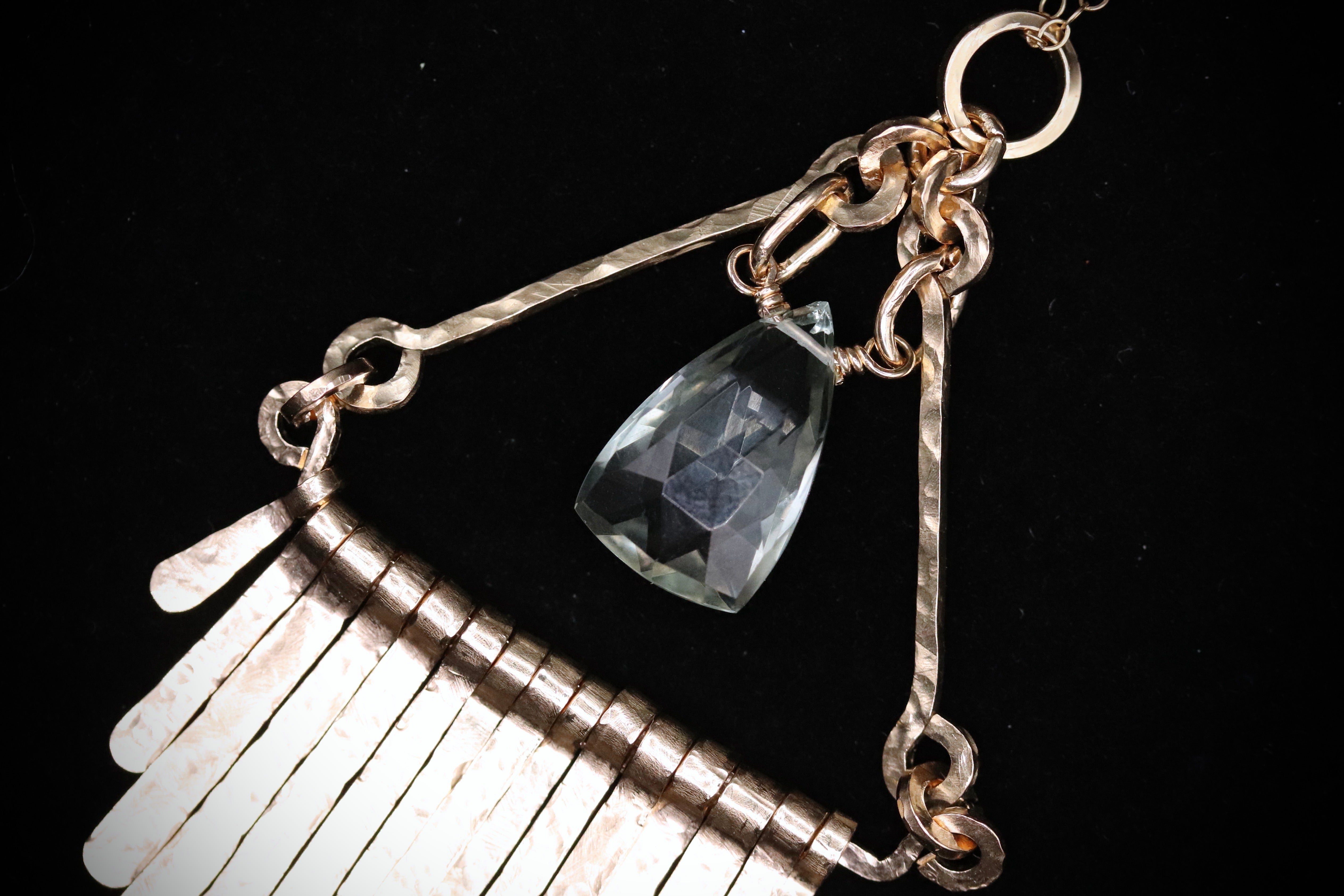 A close-up view of a delicate necklace with a clear gemstone pendant, set against a dark background.
