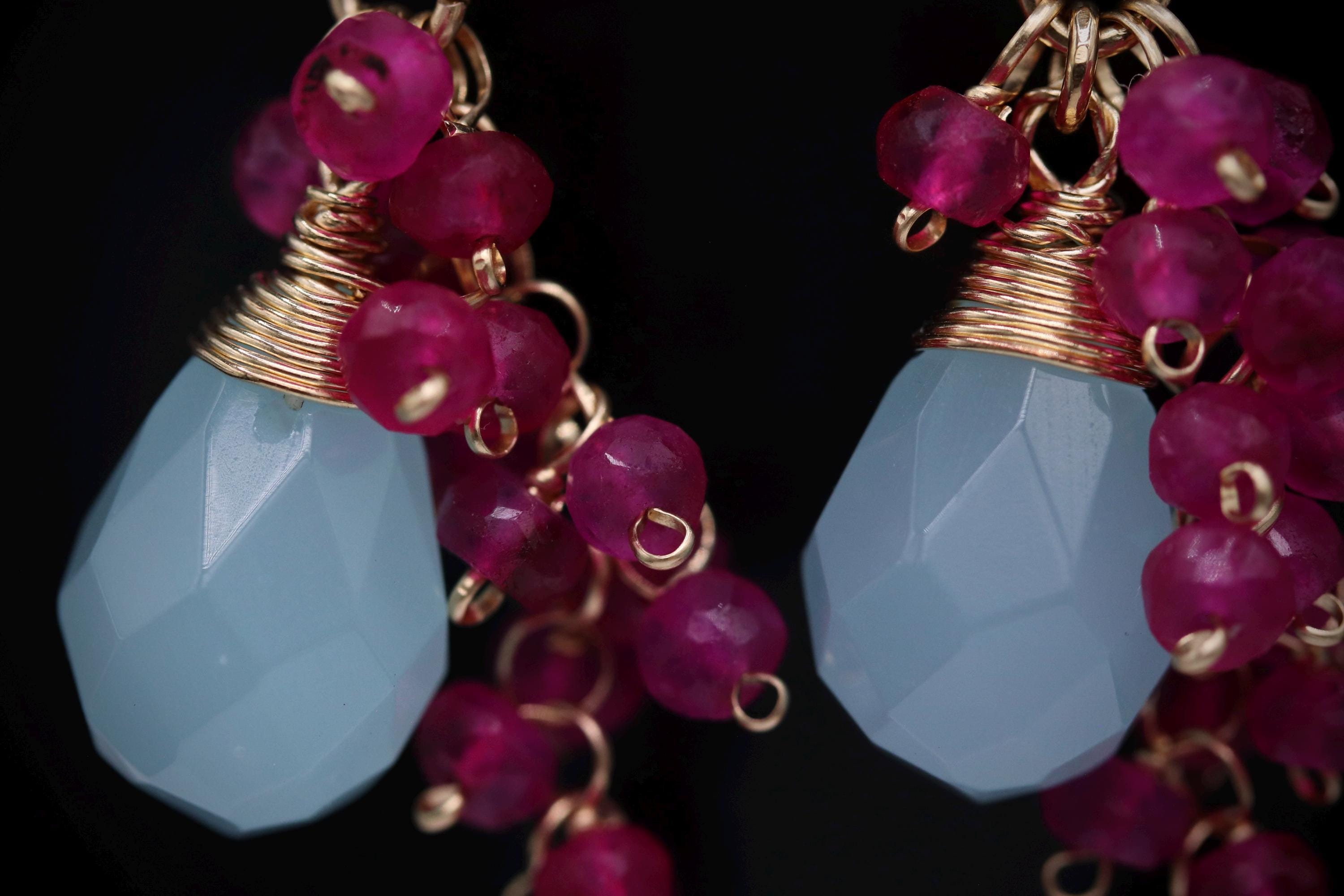 A close-up image of a pair of earrings with a combination of blue and red gemstones, as well as gold-colored metal elements.