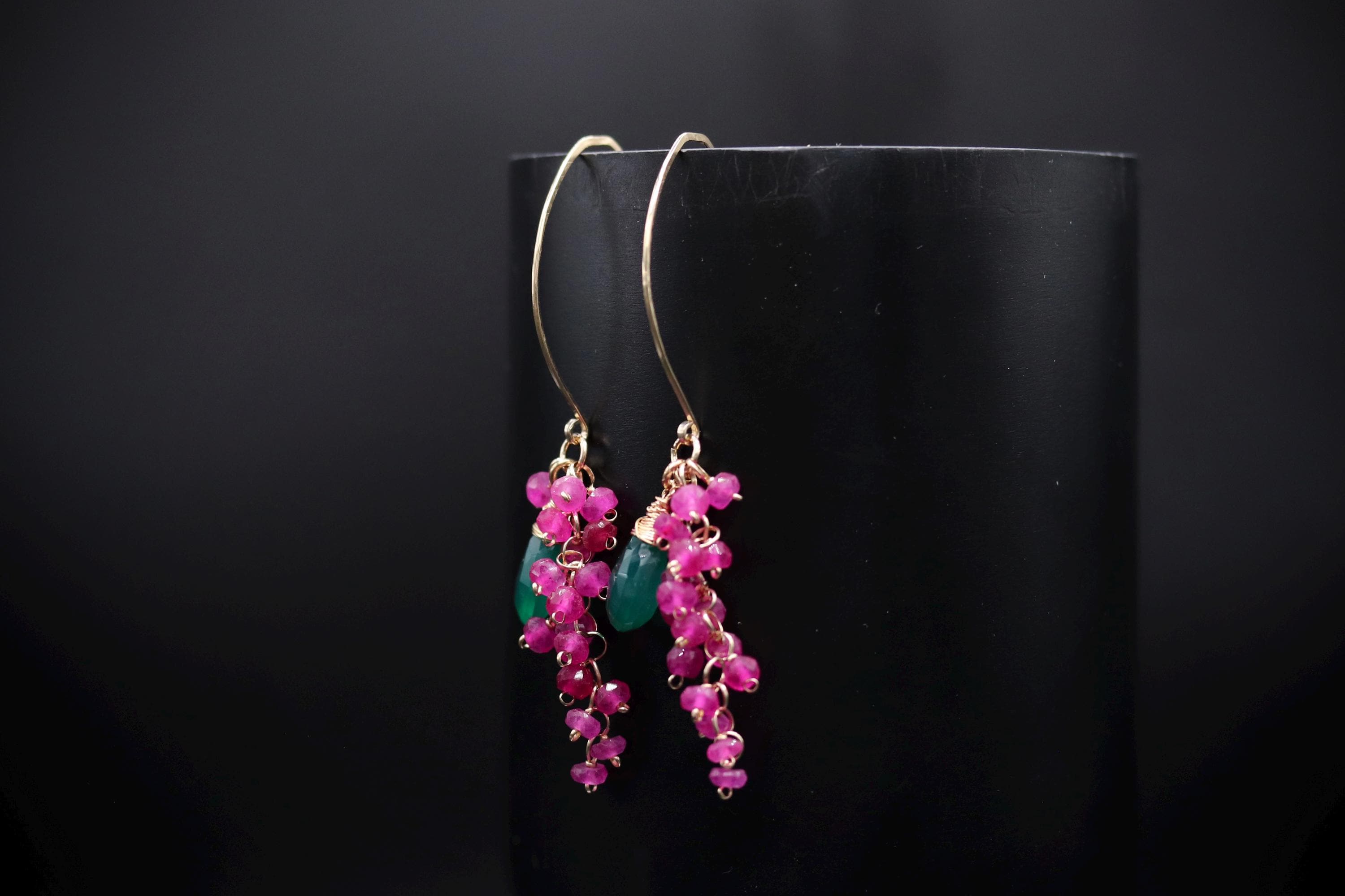 A pair of earrings with green and pink gemstones hanging from a black background.