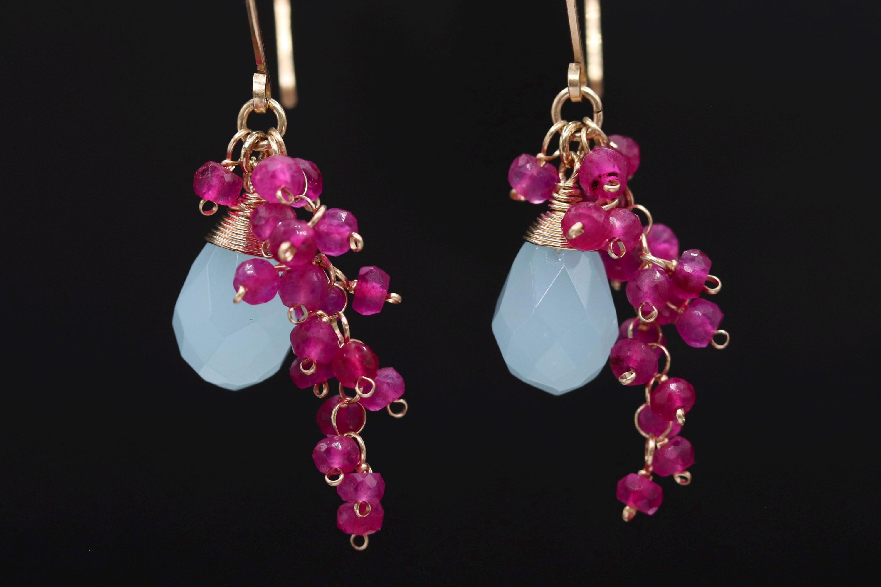 A pair of earrings with blue and pink gemstones and dangling charms.