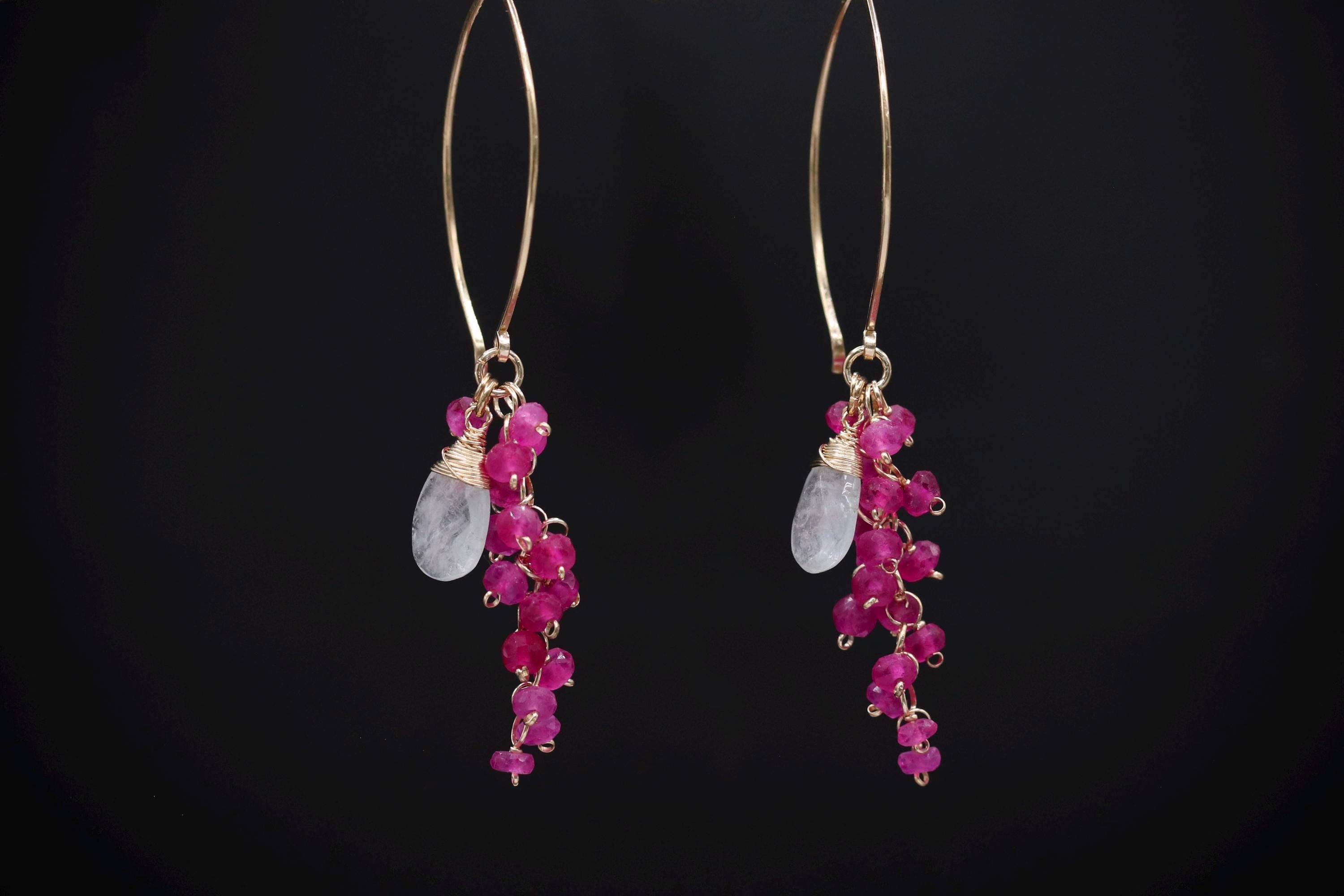 A pair of gold hoop earrings with a combination of pink gemstones and clear gemstones hanging from the bottom.