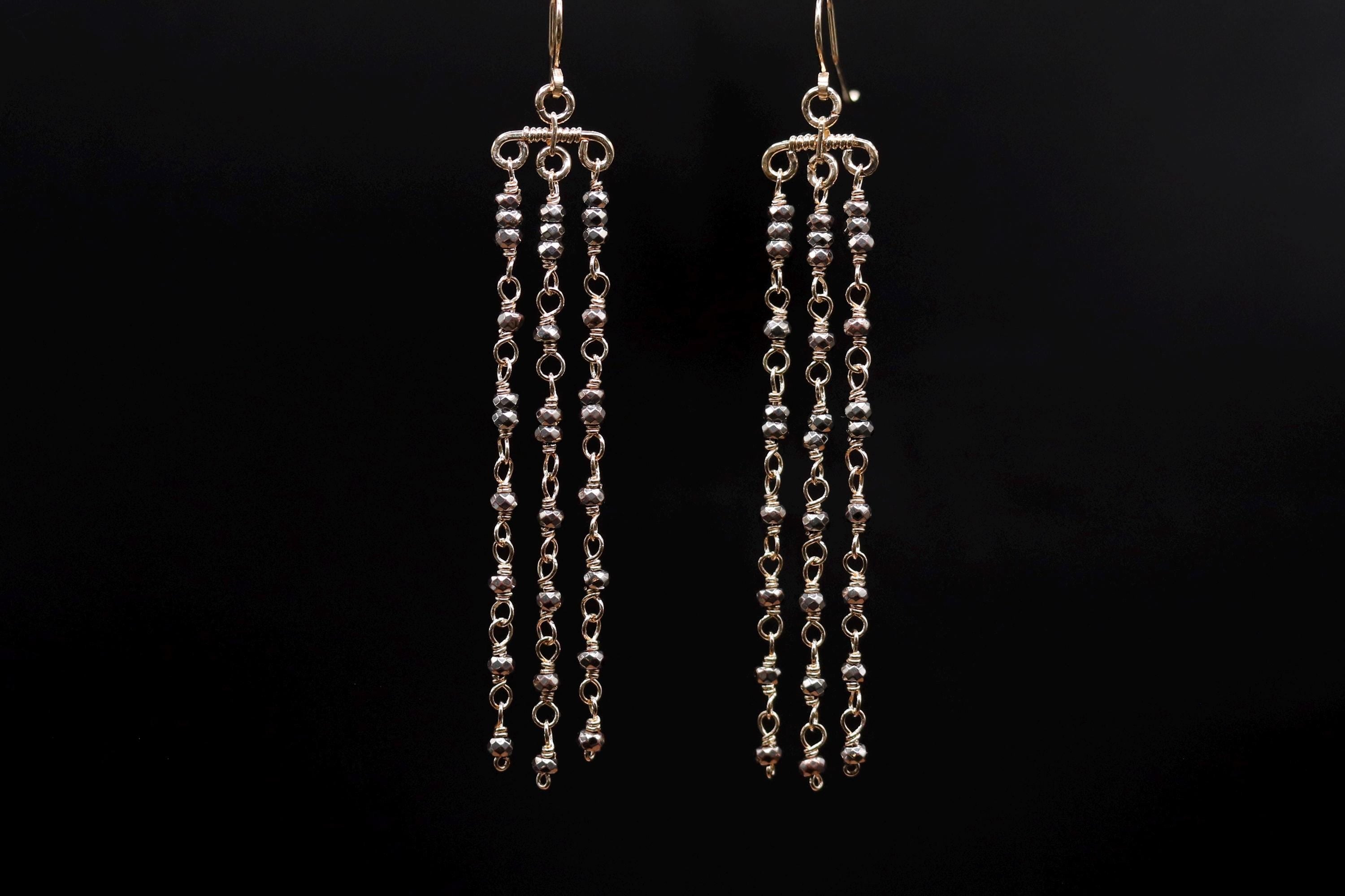 A pair of gold earrings with long, dangling chains against a black background.