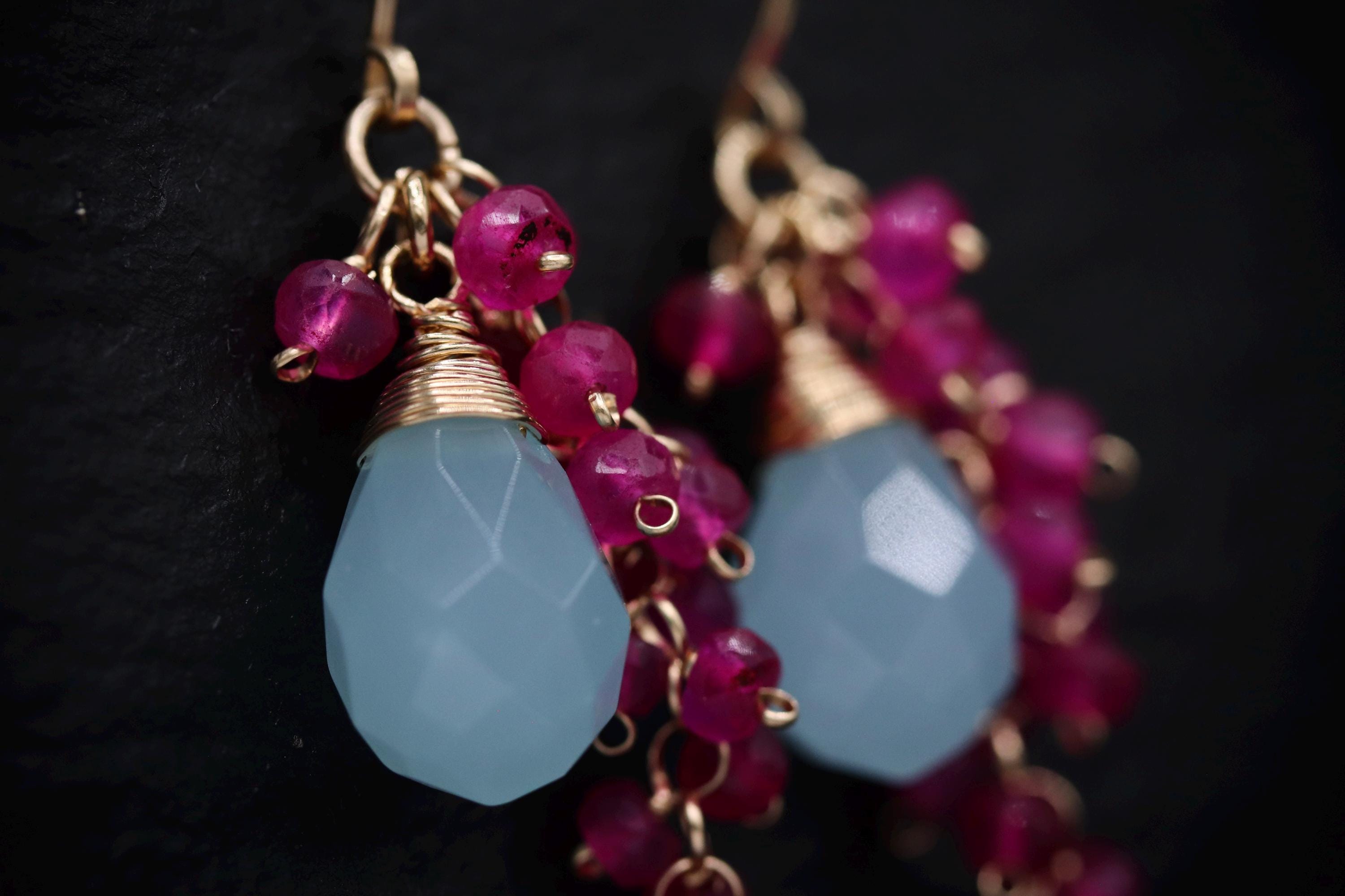 A close-up view of a pair of earrings with a combination of blue and pink gemstones, as well as small, dangling beads.