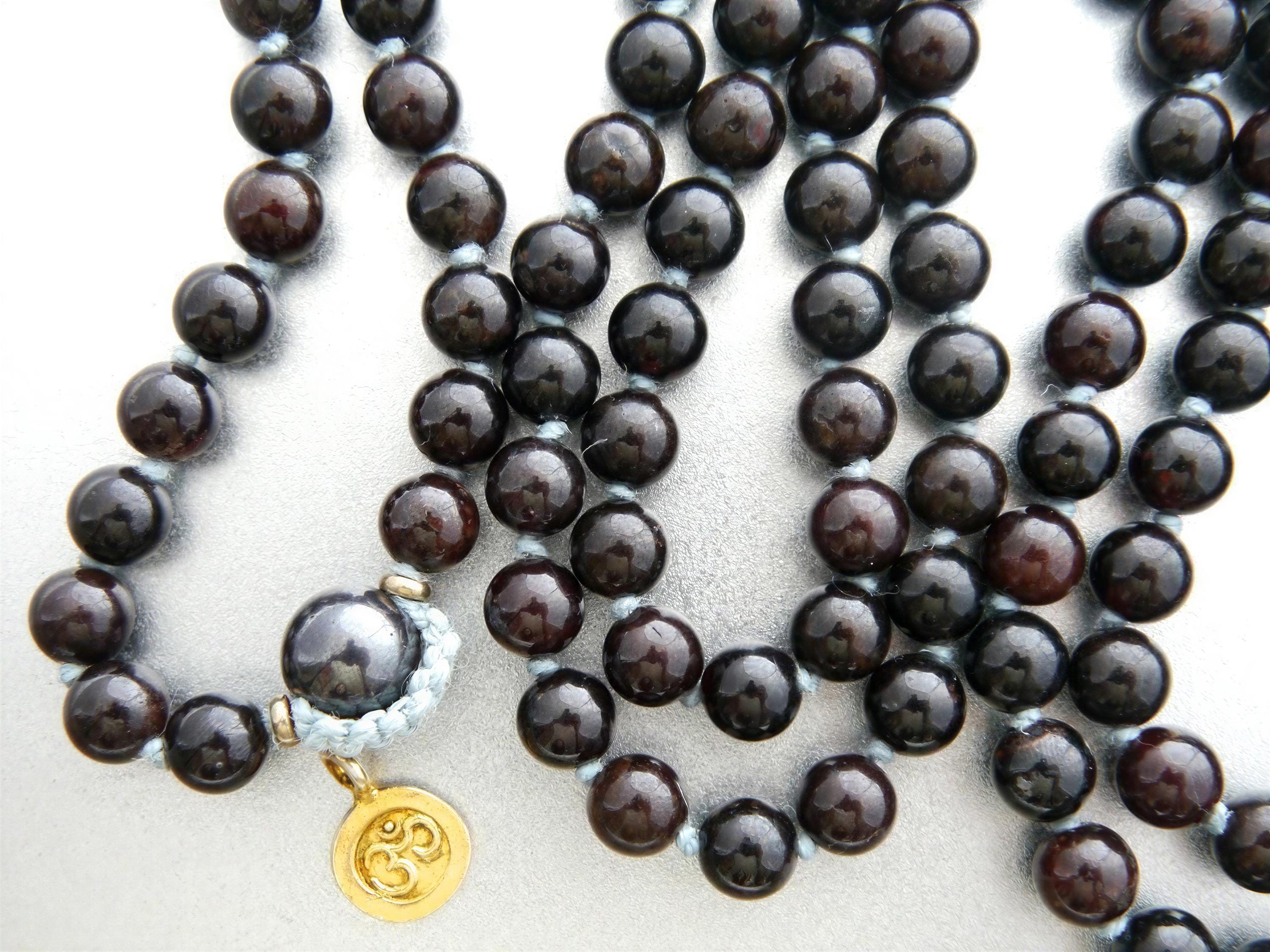 A close-up image of a beaded necklace with dark brown beads and a gold pendant featuring the Om symbol.