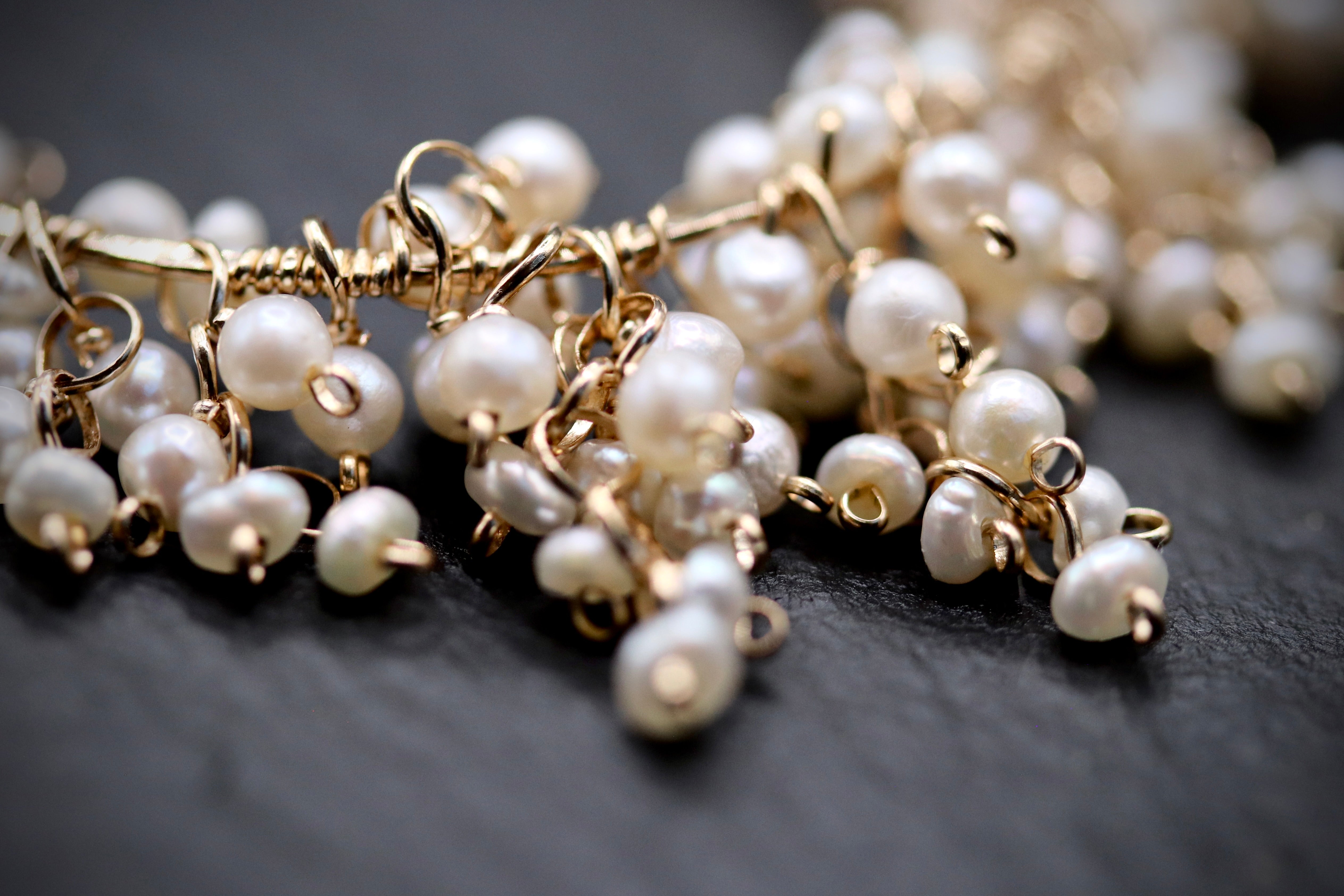 A close-up image of a delicate necklace made of numerous small, white pearls strung together with gold-colored metal.