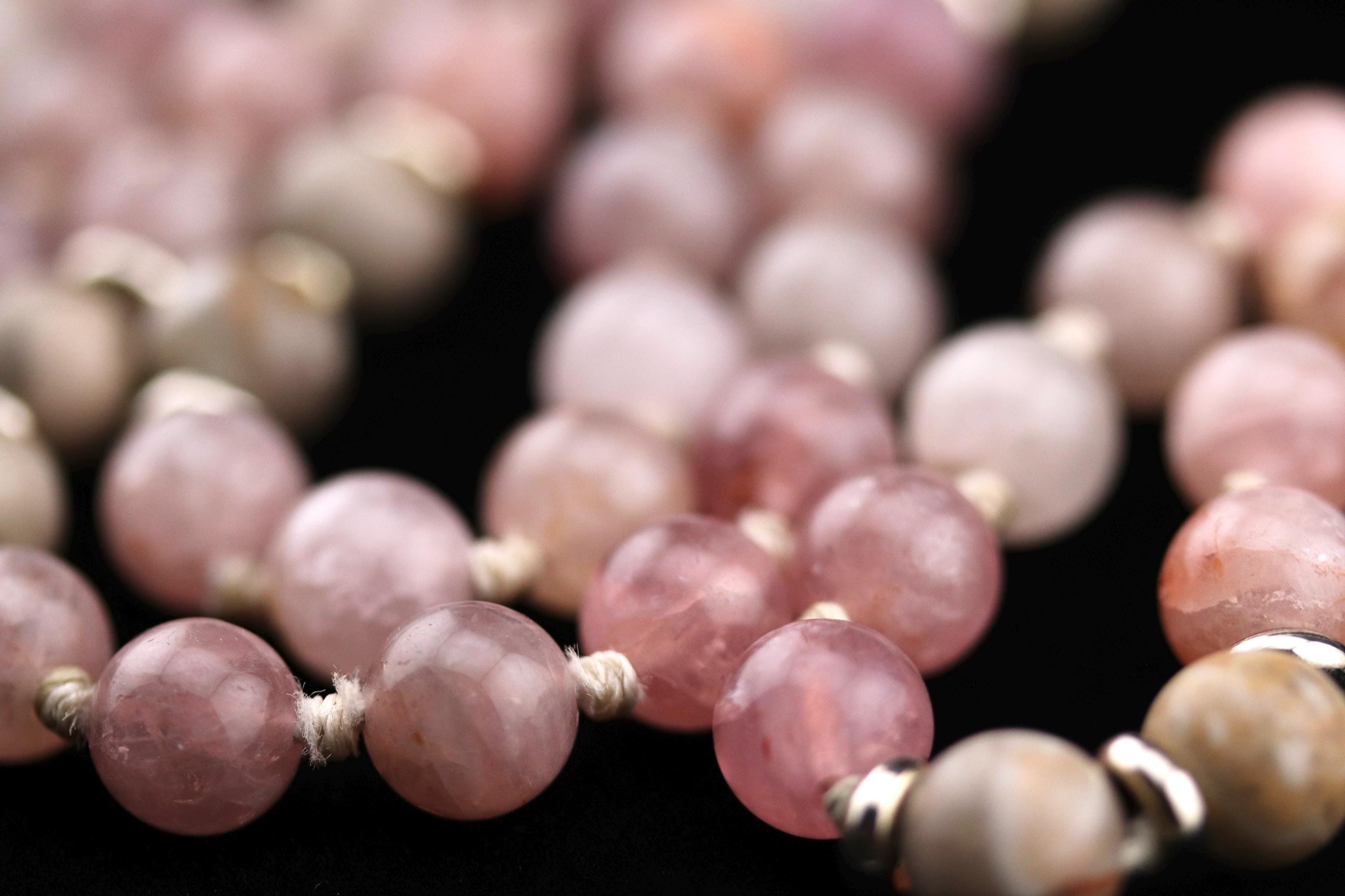 A close-up image of a collection of pink and white gemstone beads, possibly pearls or jade, arranged in a decorative pattern.