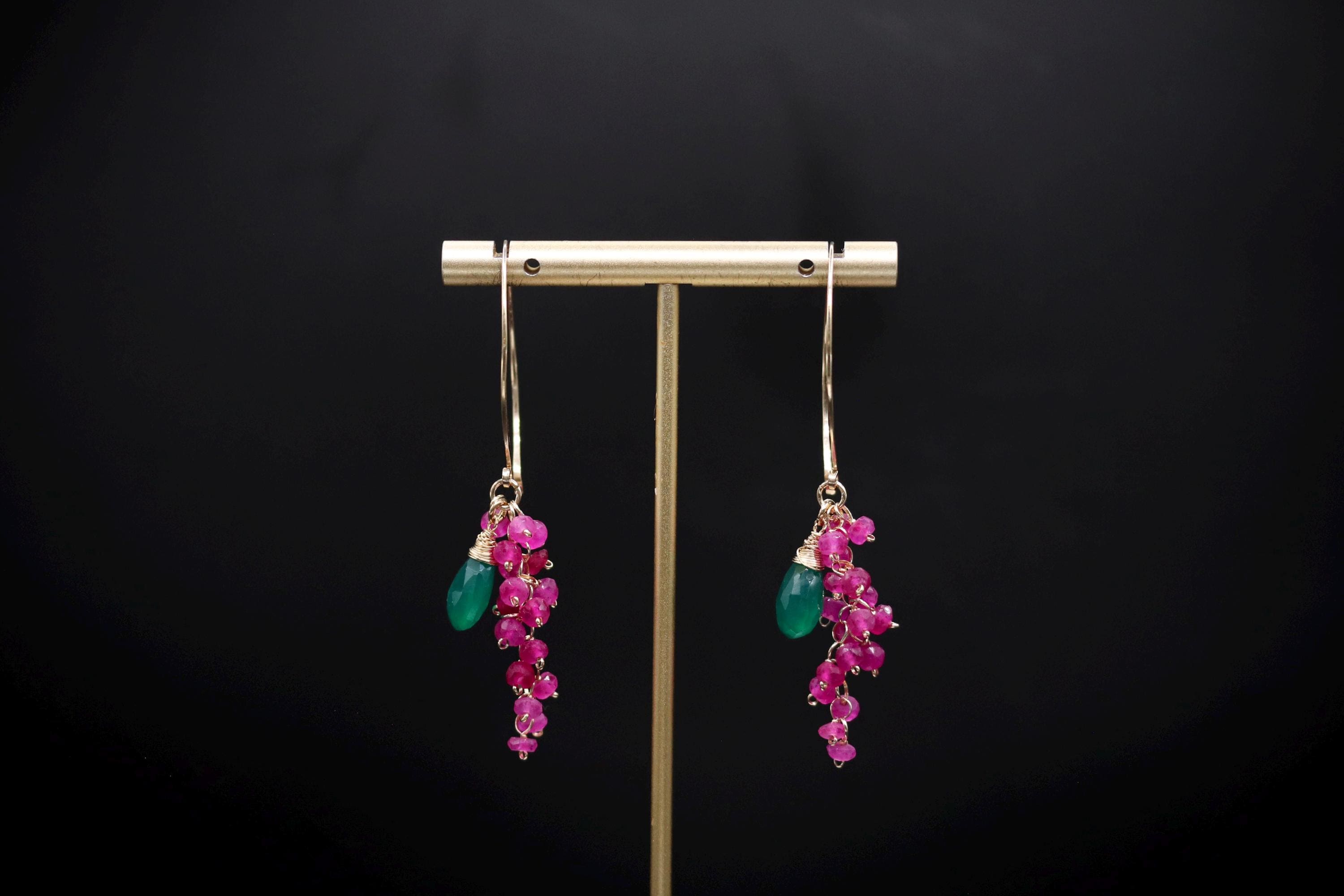 A pair of earrings with a gold metal stand and dangling earrings with green and pink gemstones.