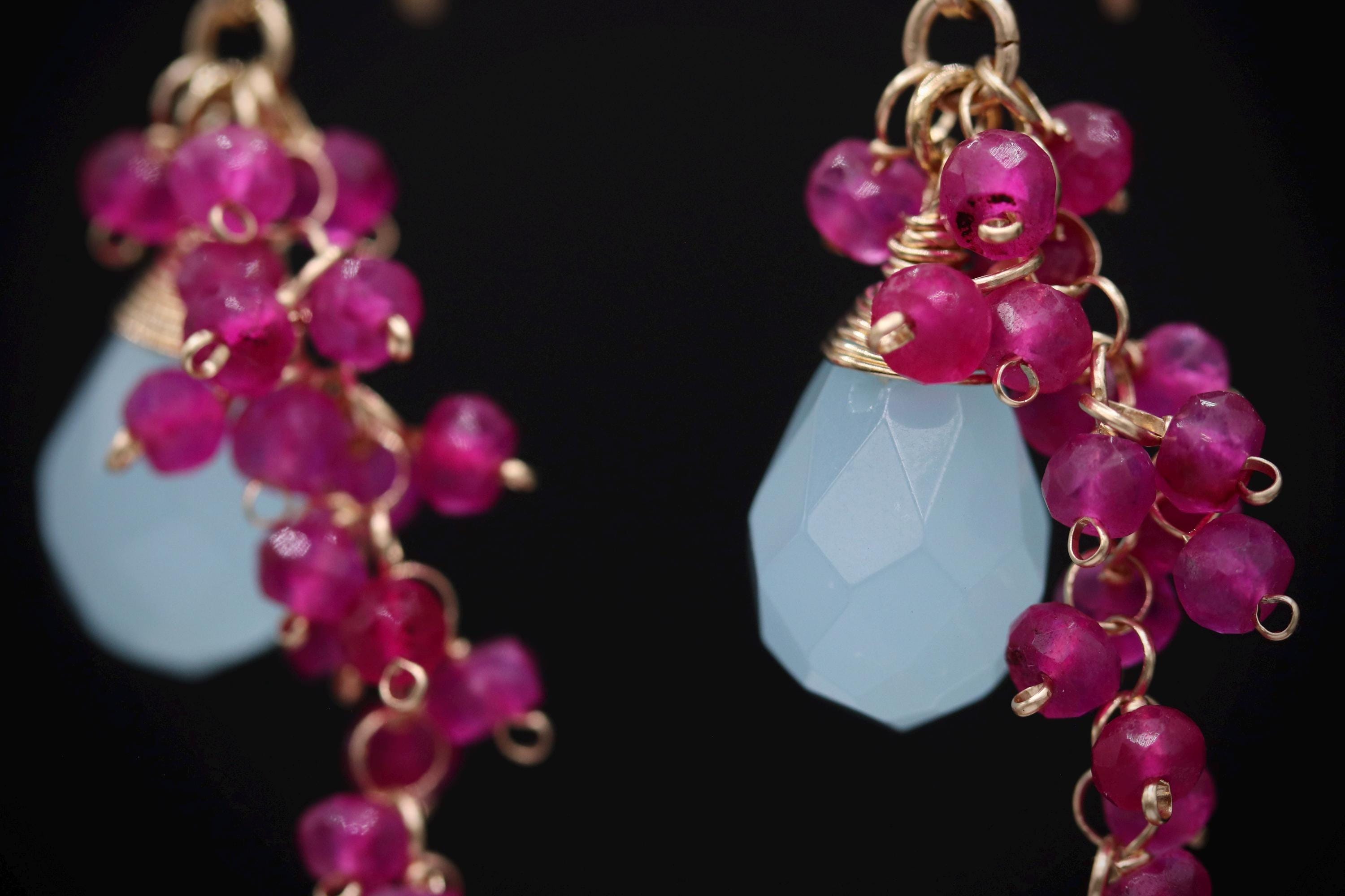 A close-up view of a pair of earrings with a combination of blue and pink gemstones, as well as gold-colored beads.