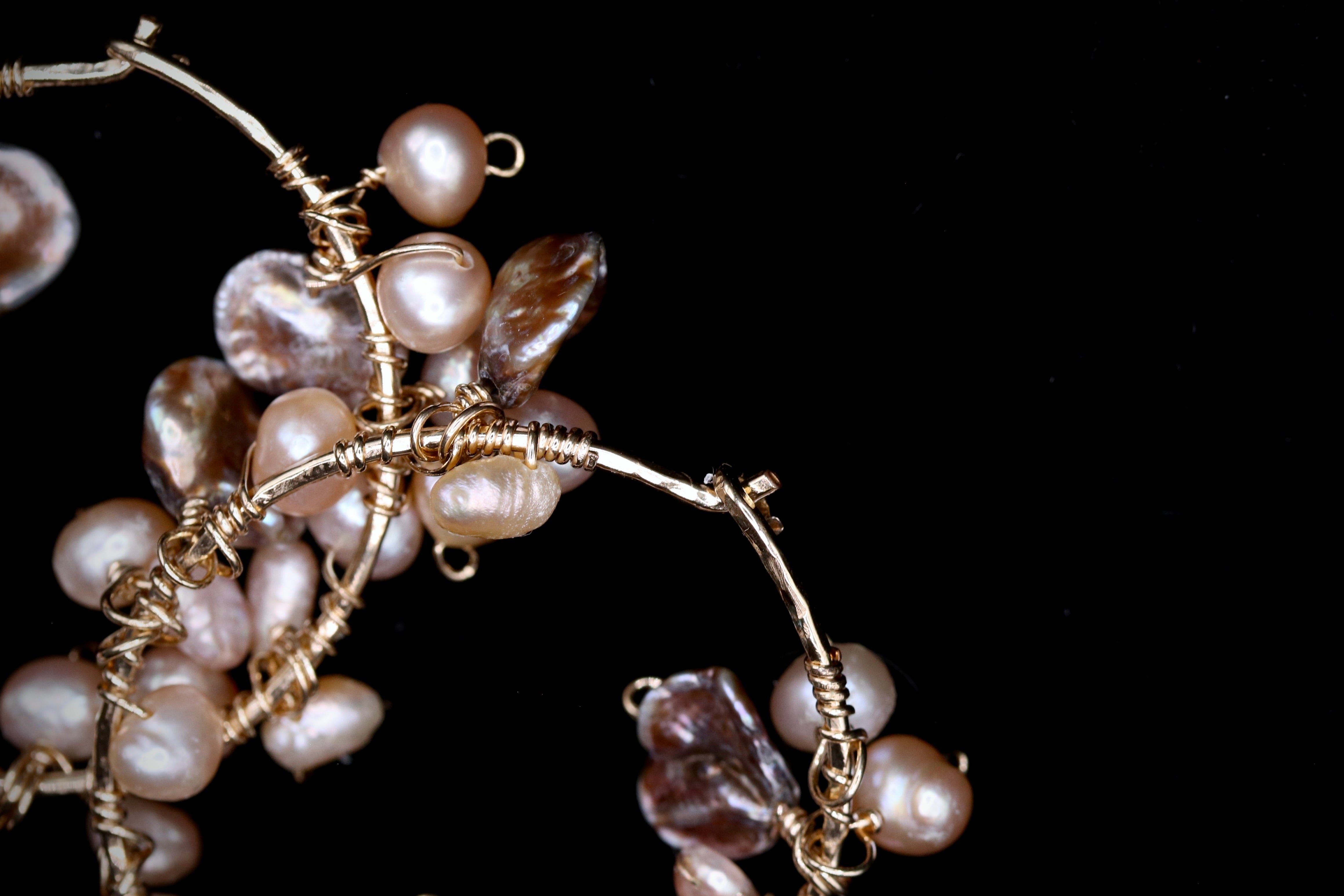 A close-up view of a delicate piece of jewelry, featuring a branch made of twisted wire and adorned with numerous small pearls in shades of white and brown.