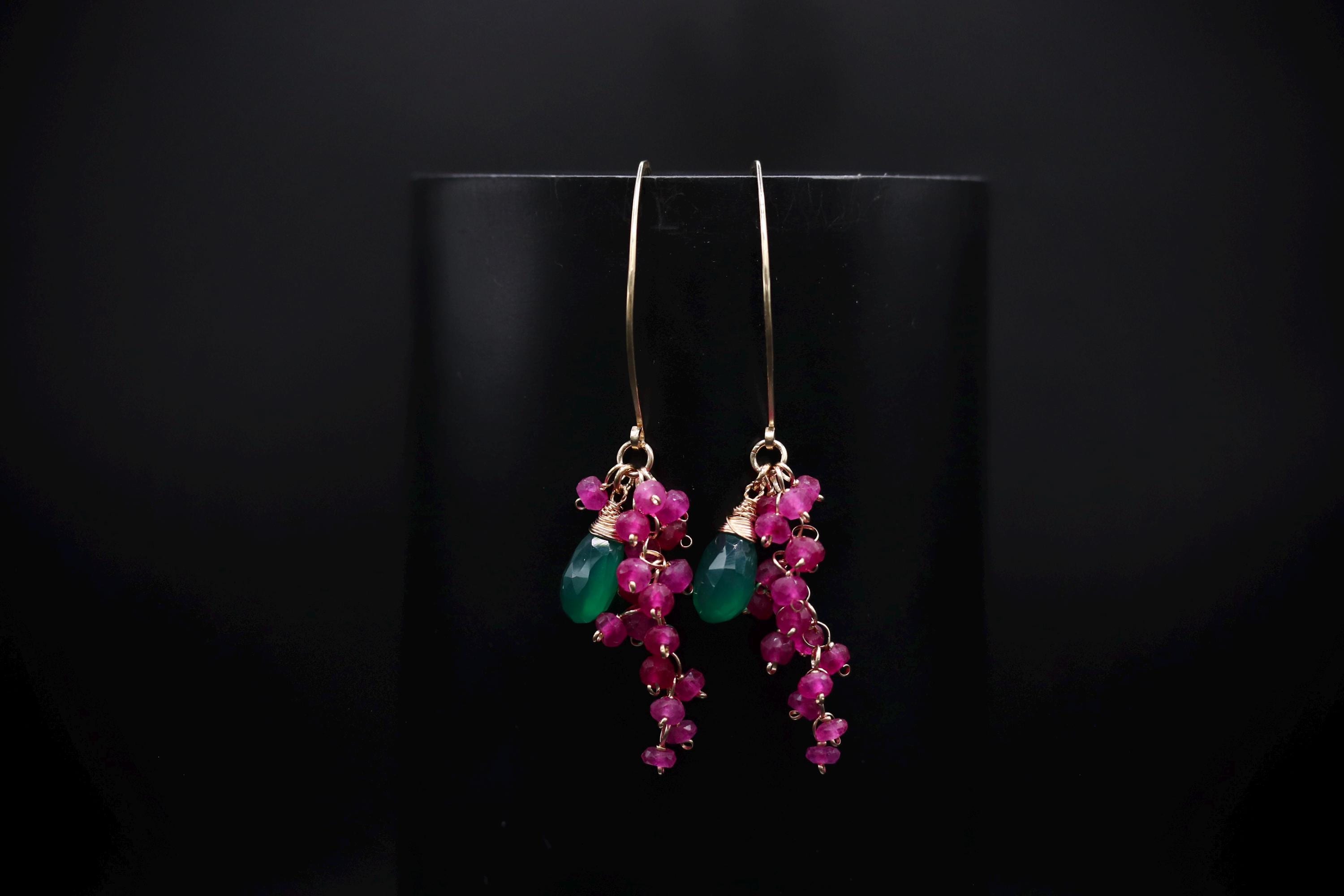 A pair of earrings with green and pink gemstones hanging from a black background.