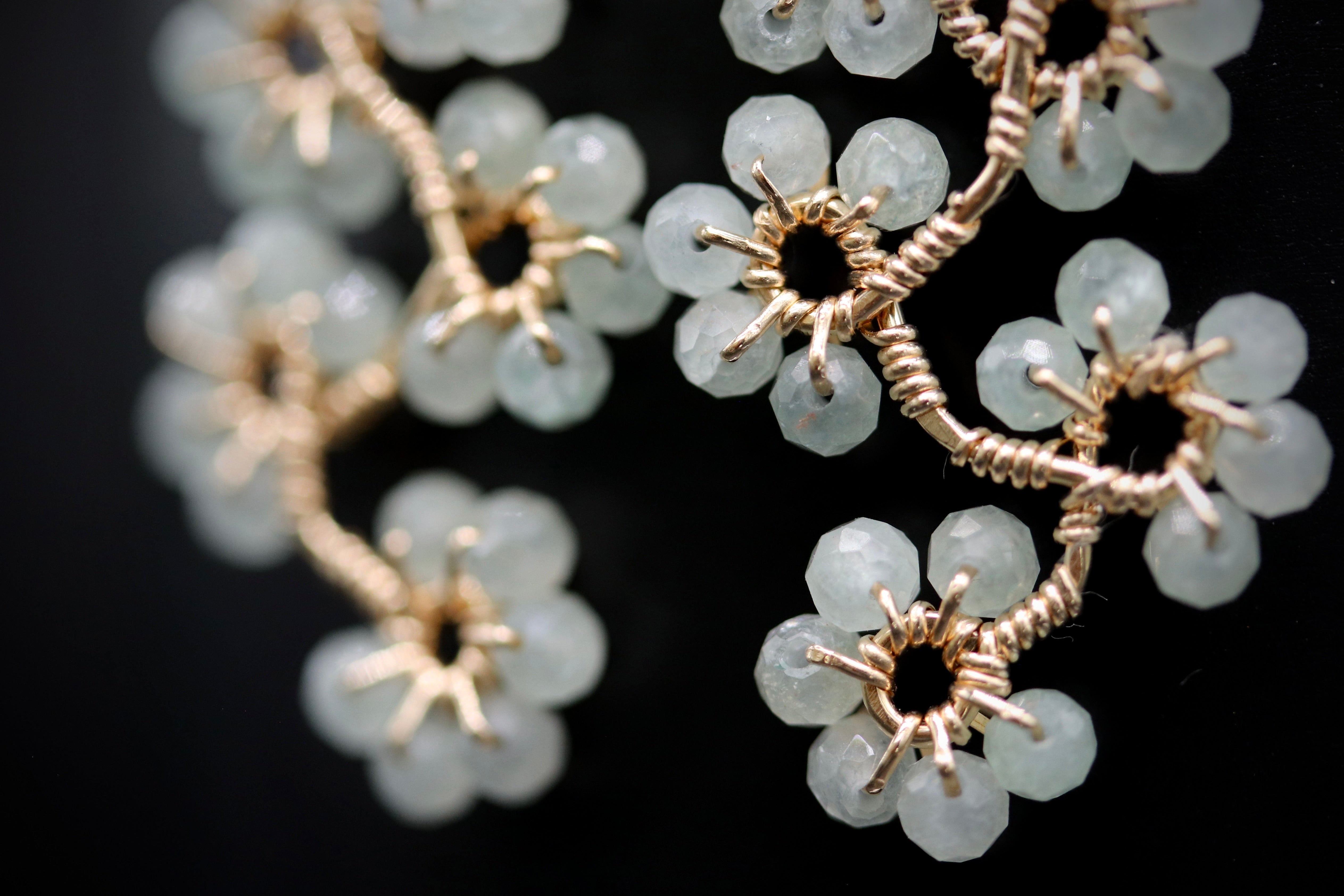 A close-up view of a delicate, intricate piece of jewelry featuring a branch-like design with small, clear gemstone-like beads arranged in a floral pattern.