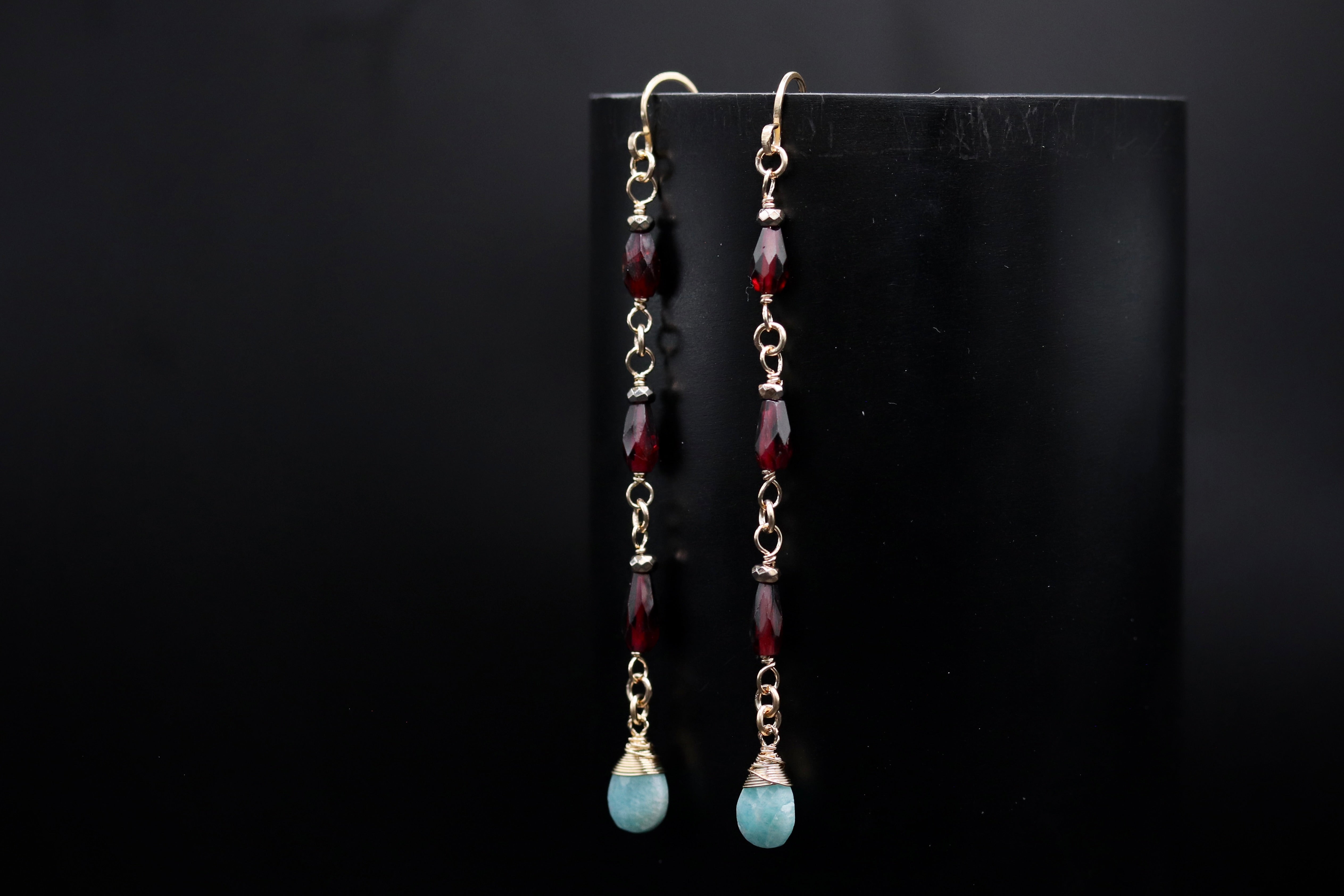 A pair of earrings with red and blue gemstones hanging from the bottom, displayed against a black background.