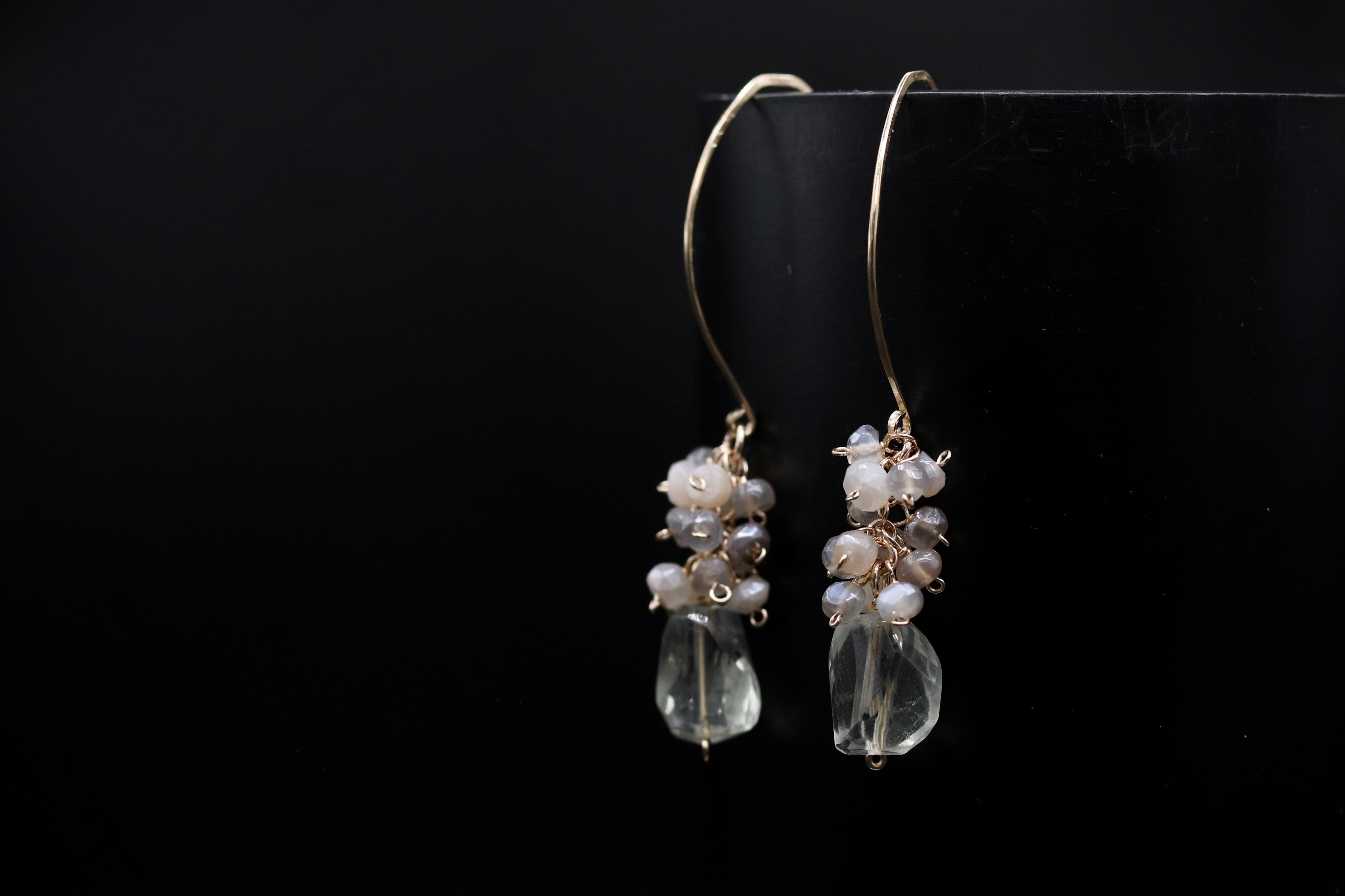 A pair of elegant earrings with clear gemstone accents and metal hooks, displayed against a black background.