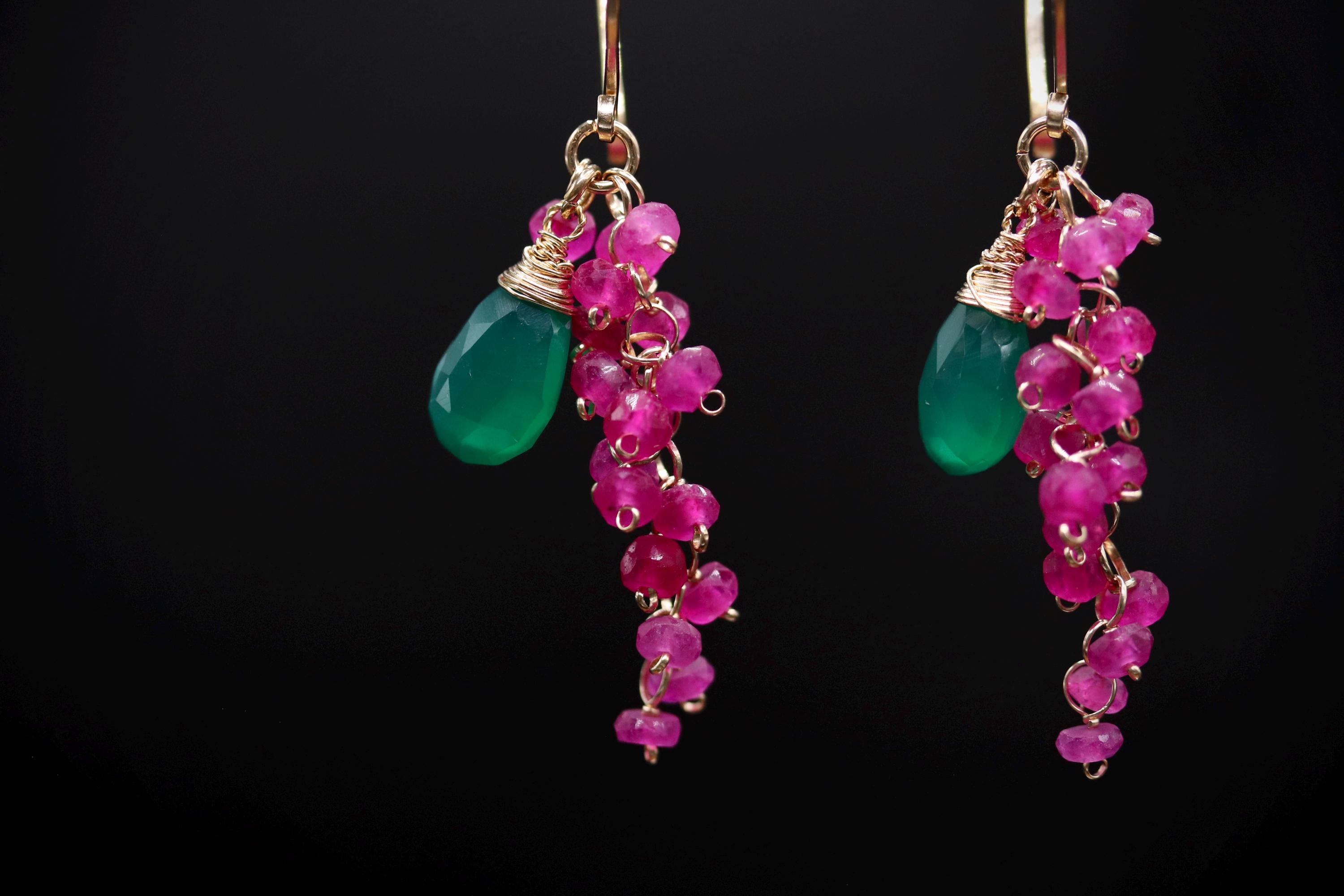 A pair of earrings with green and pink gemstones and dangling charms.