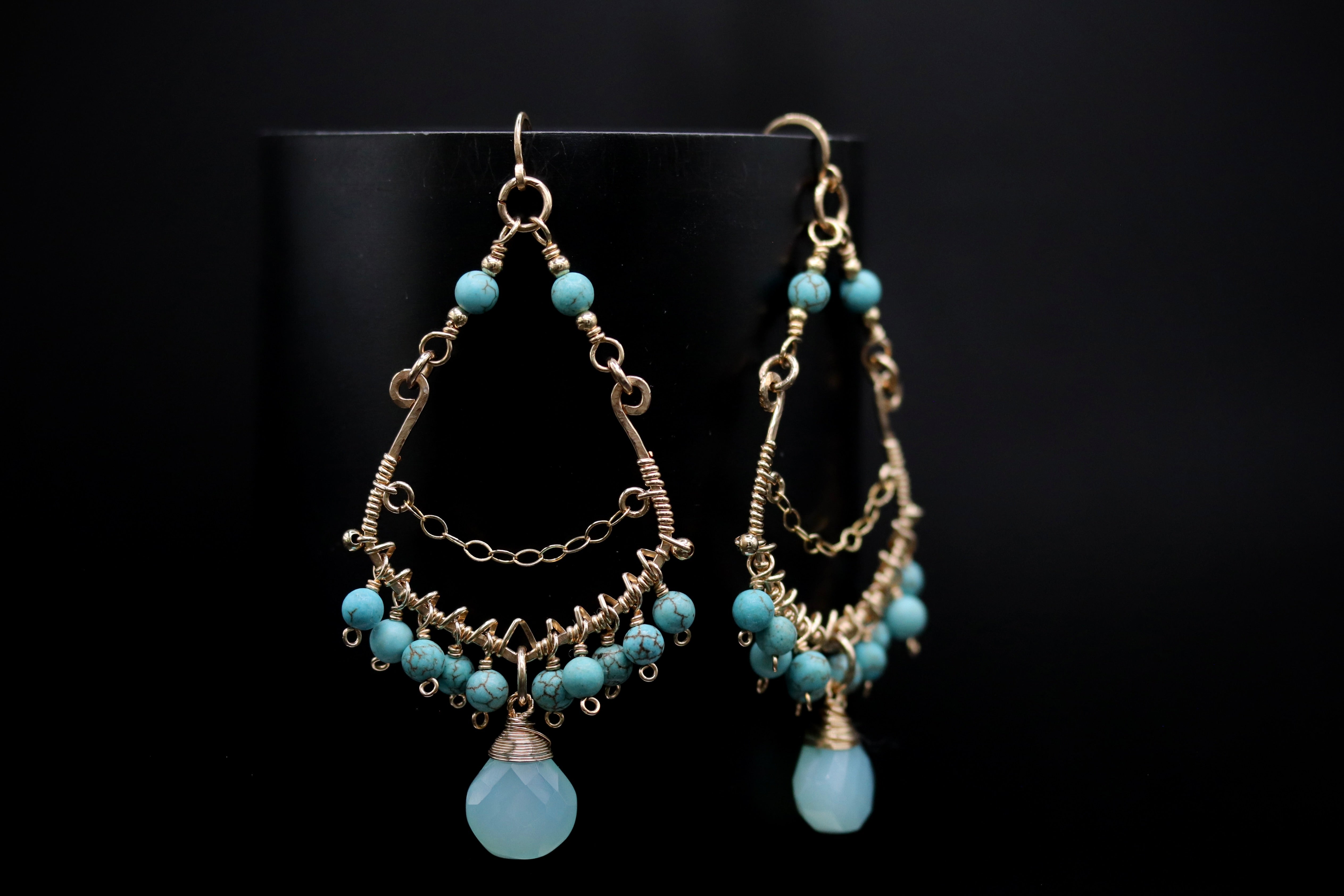 A pair of elegant earrings with turquoise stones and intricate metalwork, displayed against a black background.