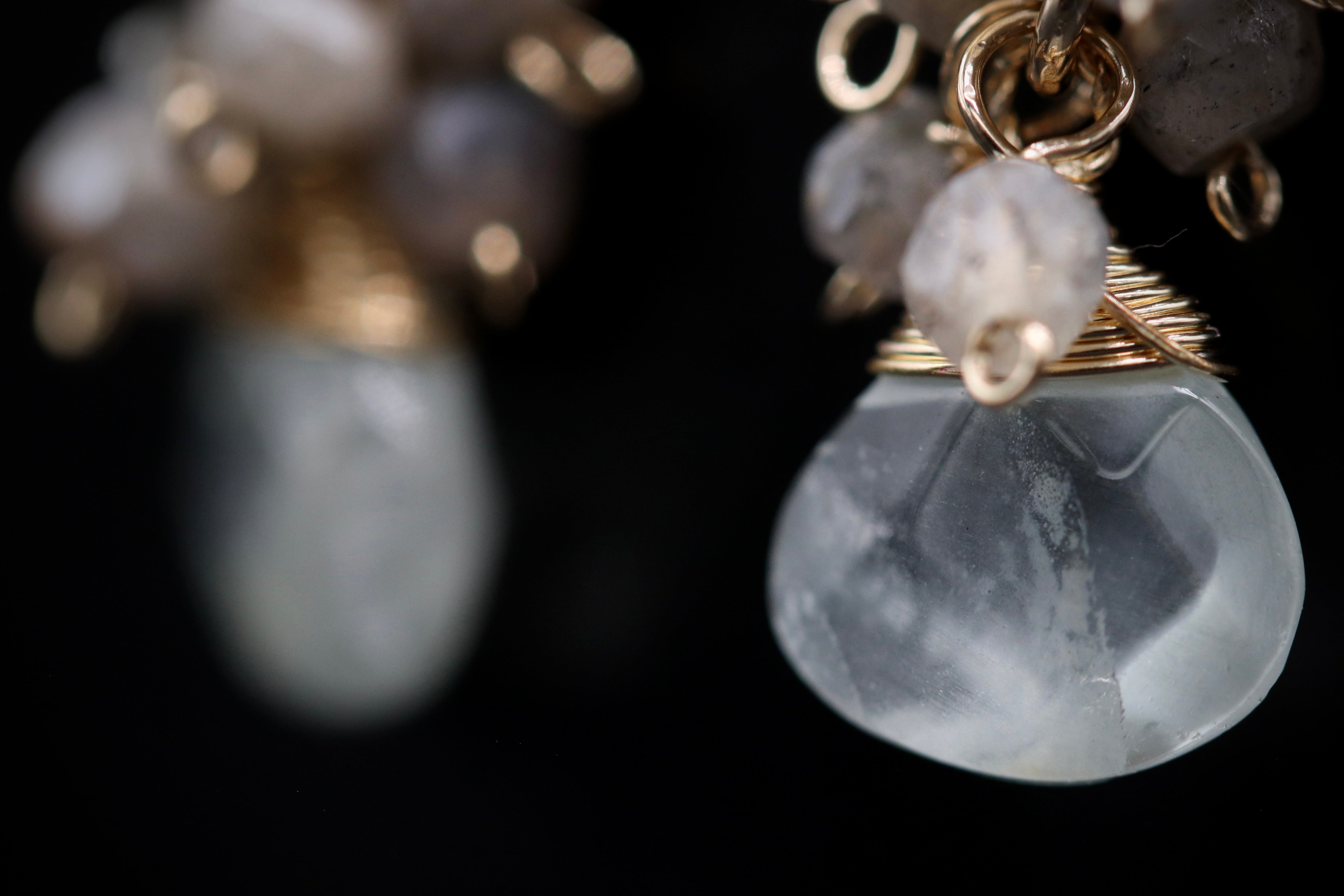A close-up view of a pair of earrings with a clear stone pendant and a gold-colored metal clasp.