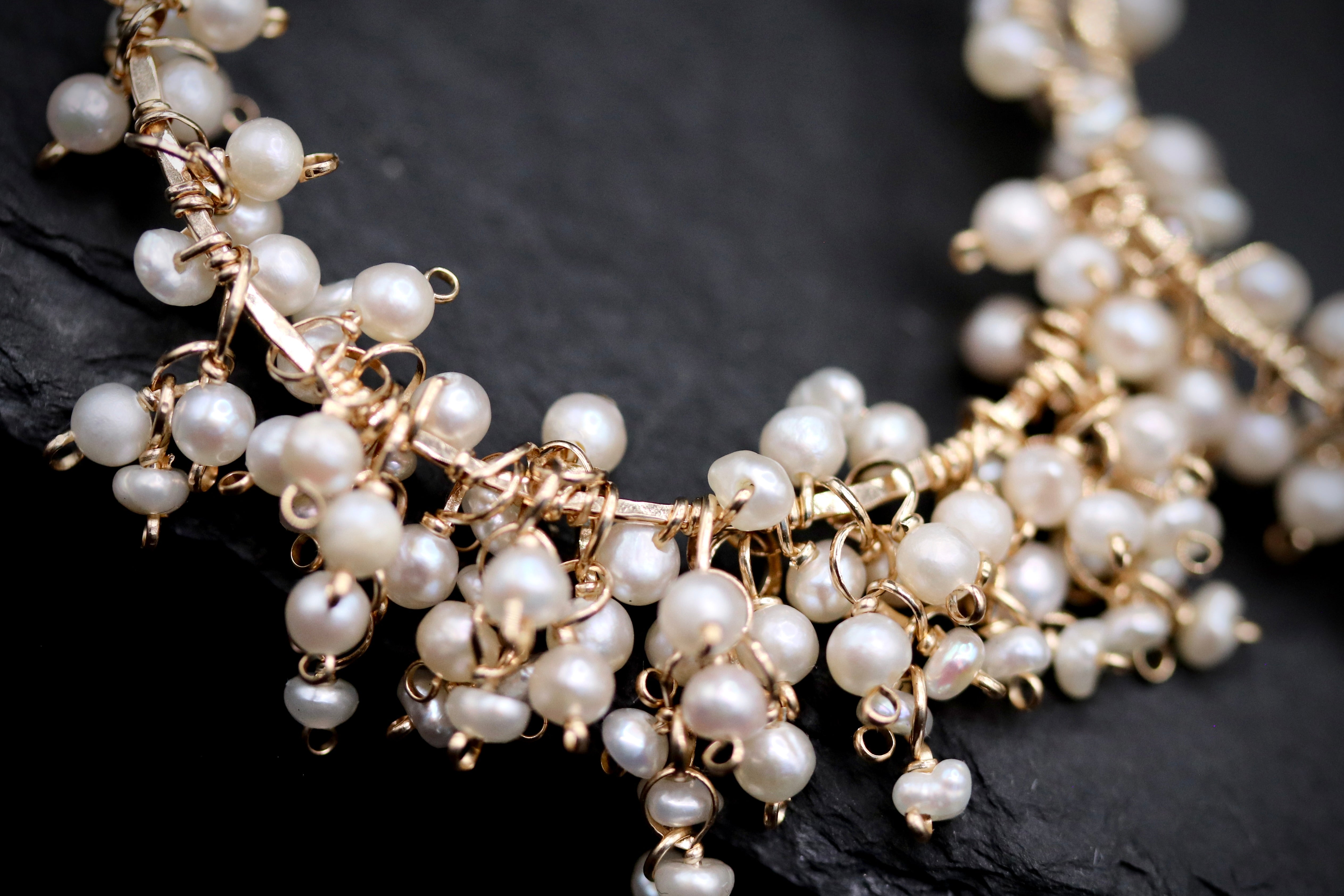 A close-up image of a delicate necklace with numerous small white pearls and gold-colored metal elements.