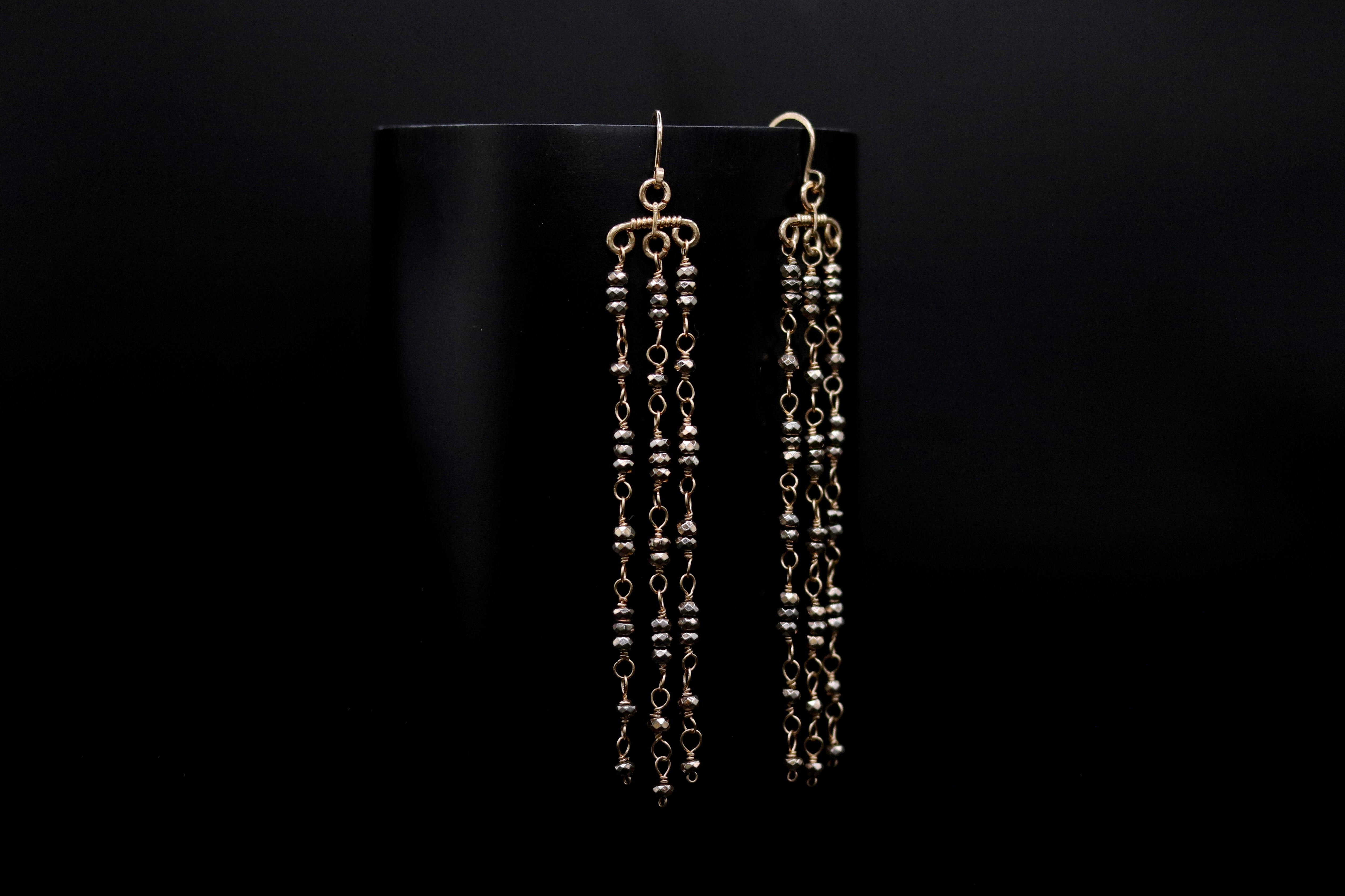 A pair of gold earrings with long, dangling chains against a black background.