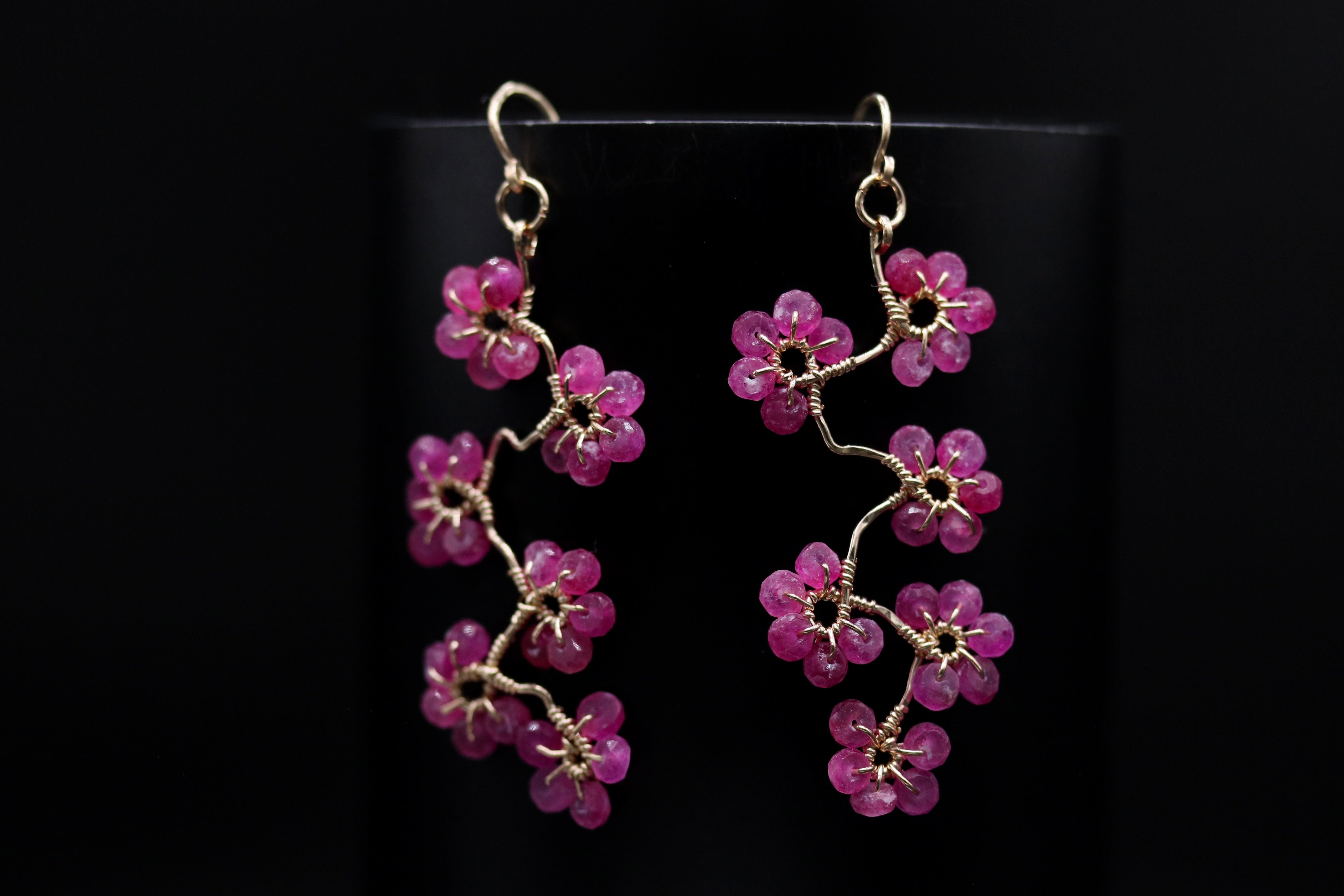 A pair of earrings with delicate pink flower-shaped charms hanging from a wire.