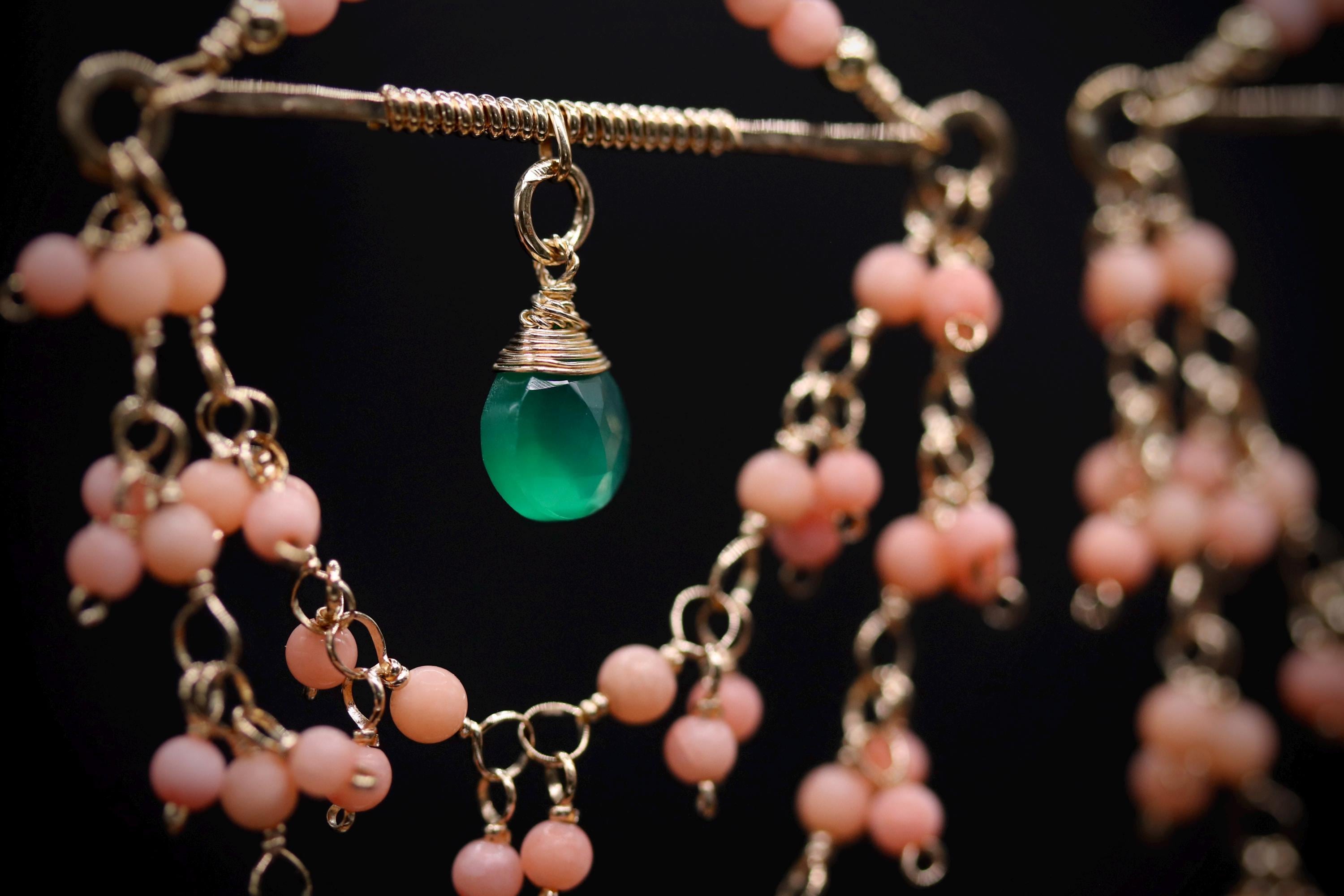 A close-up view of a necklace with a green gemstone pendant and a chain of pink beads.